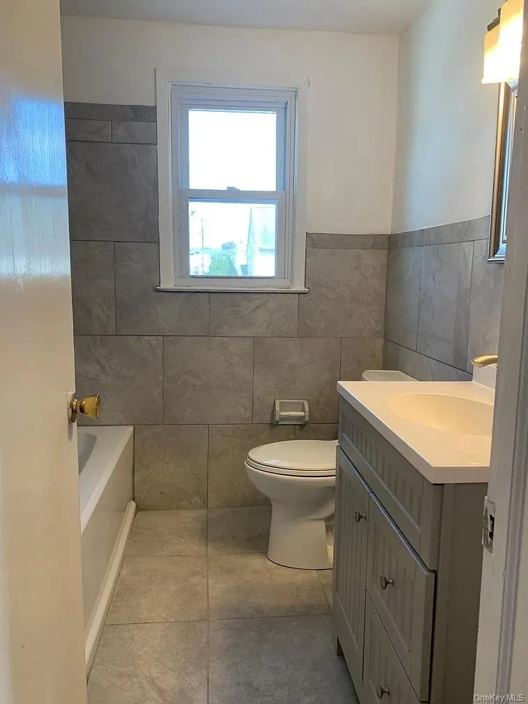 Bathroom featuring vanity, a bath, tile walls, and light tile patterned floors Bathroom featuring vanity, a bath, tile walls, and light tile patterned floors