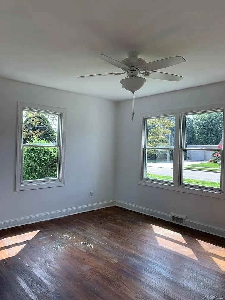 Empty room with healthy amount of natural light, dark wood-style flooring, and ceiling fan Empty room with healthy amount of natural light, dark wood-style flooring, and ceiling fan