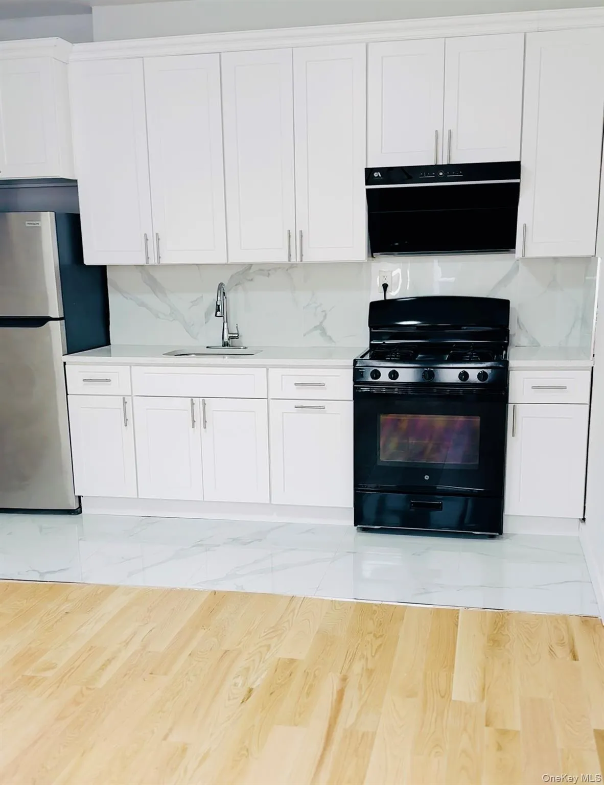 Kitchen featuring black range with gas stovetop, tasteful backsplash, white cabinets, and freestanding refrigerator Kitchen featuring black range with gas stovetop, tasteful backsplash, white cabinets, and freestanding refrigerator