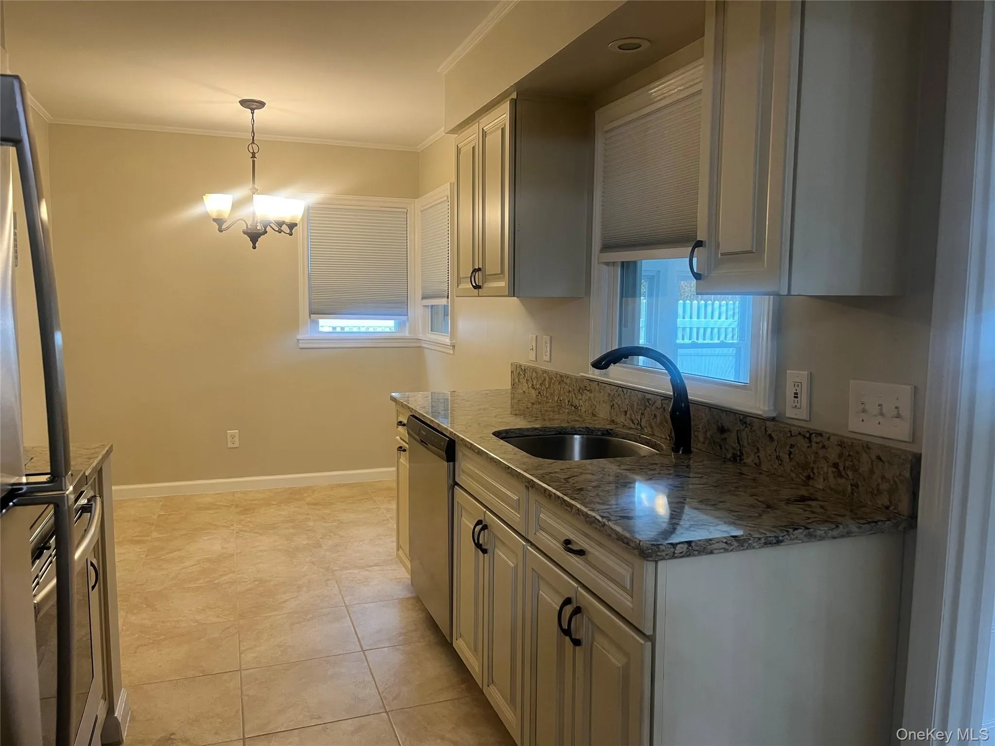 Kitchen featuring dark stone countertops, ornamental molding, hanging light fixtures, stainless steel appliances, and a chandelier Kitchen featuring dark stone countertops, ornamental molding, hanging light fixtures, stainless steel appliances, and a chandelier