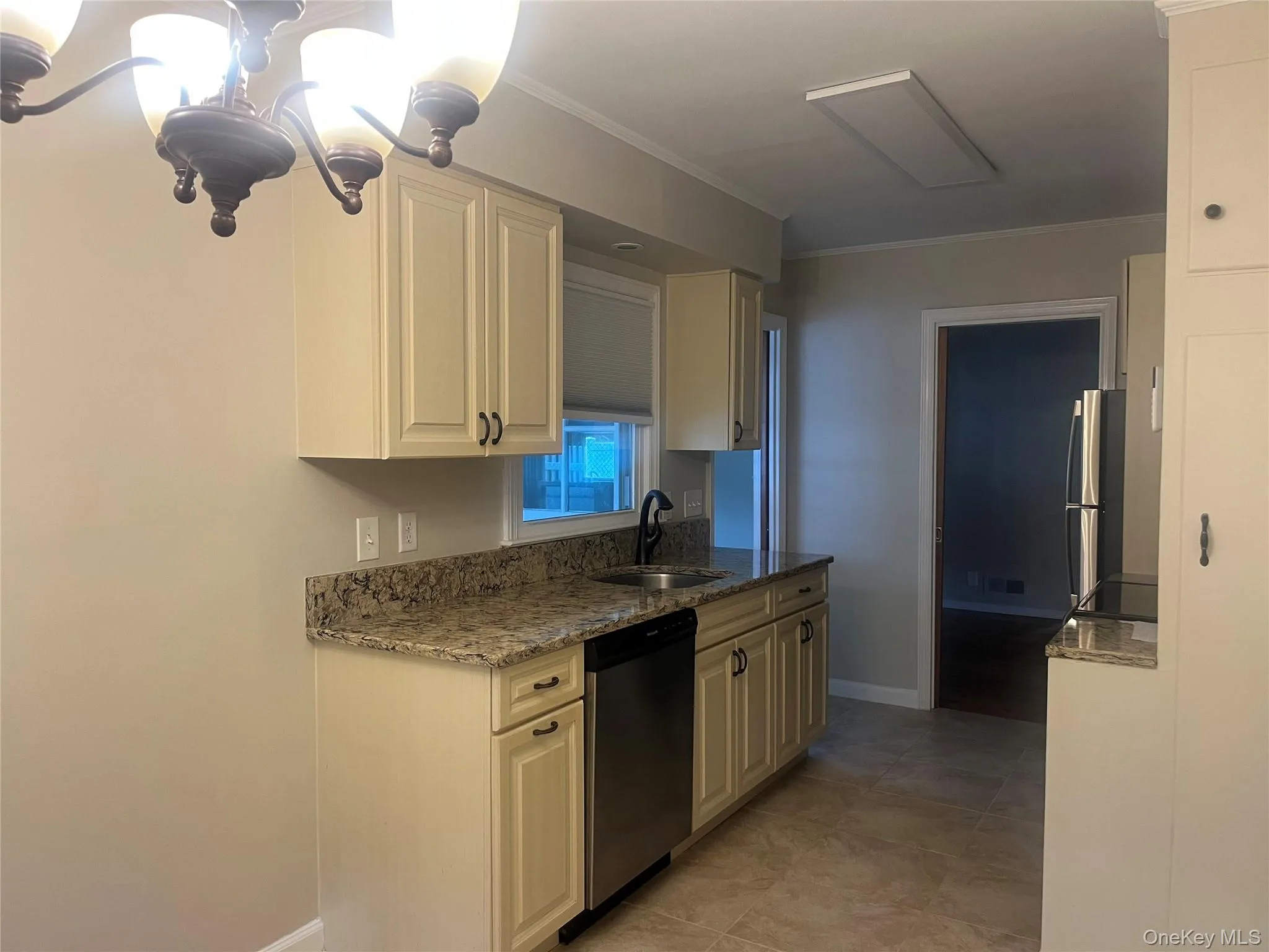 Kitchen with dark stone countertops, appliances with stainless steel finishes, ornamental molding, light tile patterned floors, and a chandelier. Space for kitchen table as well Kitchen with dark stone countertops, appliances with stainless steel finishes, ornamental molding, light tile patterned floors, and a chandelier. Space for kitchen table as well