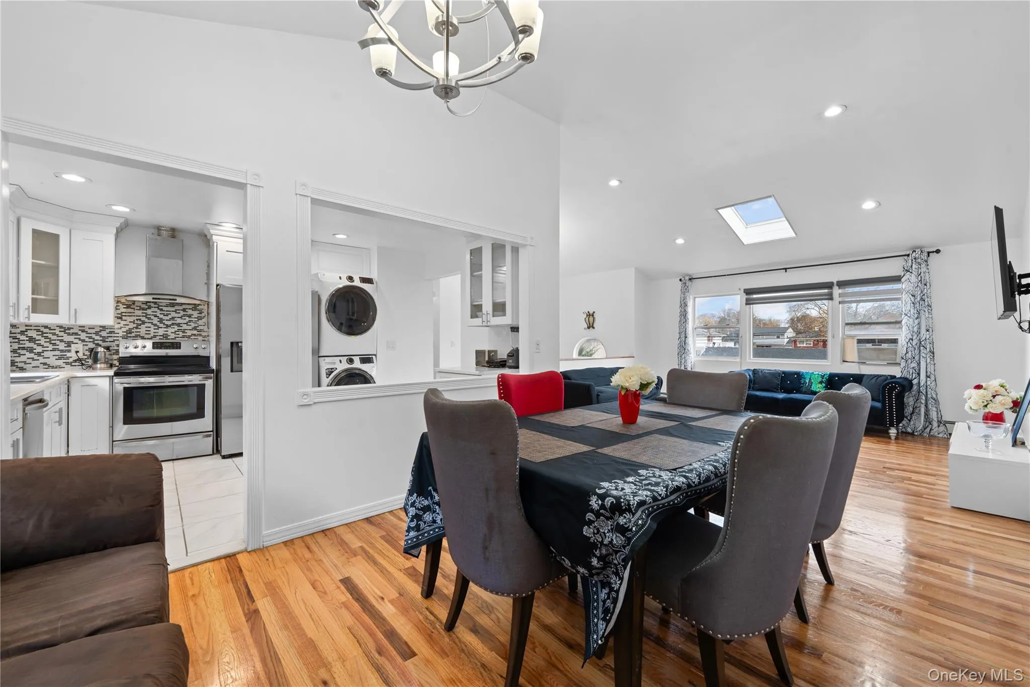 Dining area featuring a skylight, vaulted ceiling, estacked washer and dryer, light wood-type flooring, and a chandelier Dining area featuring a skylight, vaulted ceiling, estacked washer and dryer, light wood-type flooring, and a chandelier