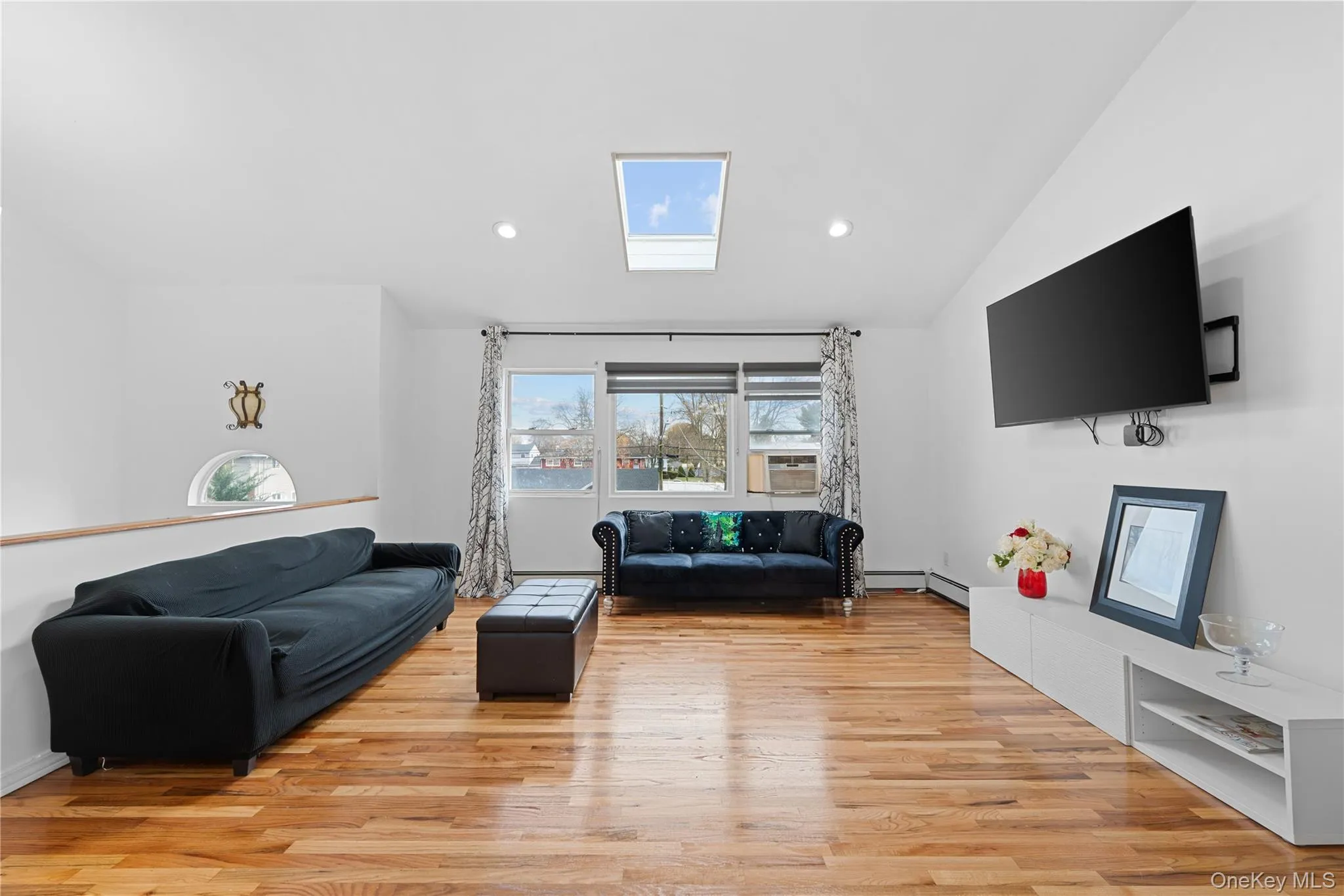 Living area featuring a skylight, light wood-style flooring, recessed lighting, vaulted ceiling, and cooling unit Living area featuring a skylight, light wood-style flooring, recessed lighting, vaulted ceiling, and cooling unit
