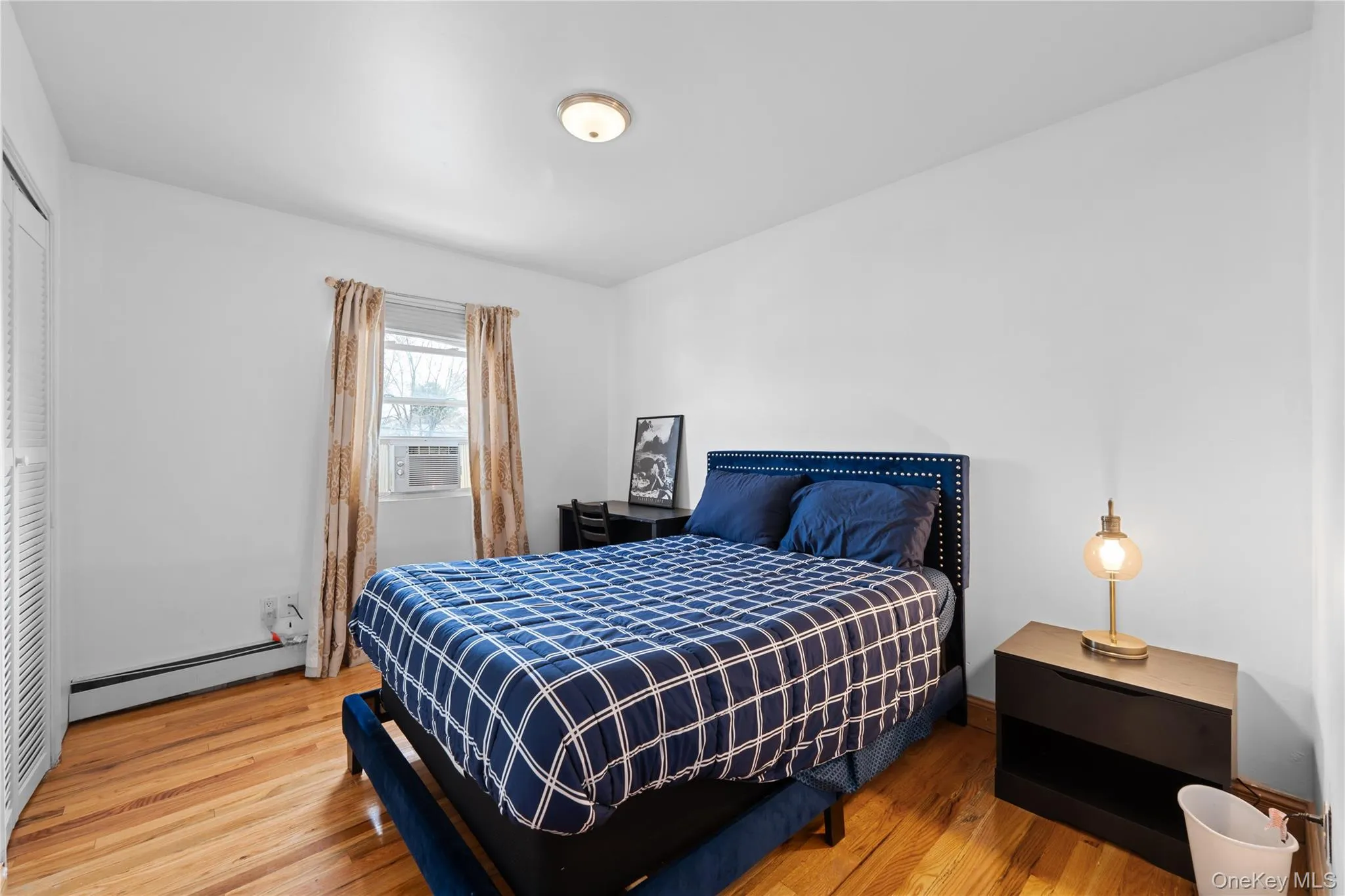 Bedroom featuring a baseboard heating unit, light wood-style flooring, a closet, and cooling unit Bedroom featuring a baseboard heating unit, light wood-style flooring, a closet, and cooling unit