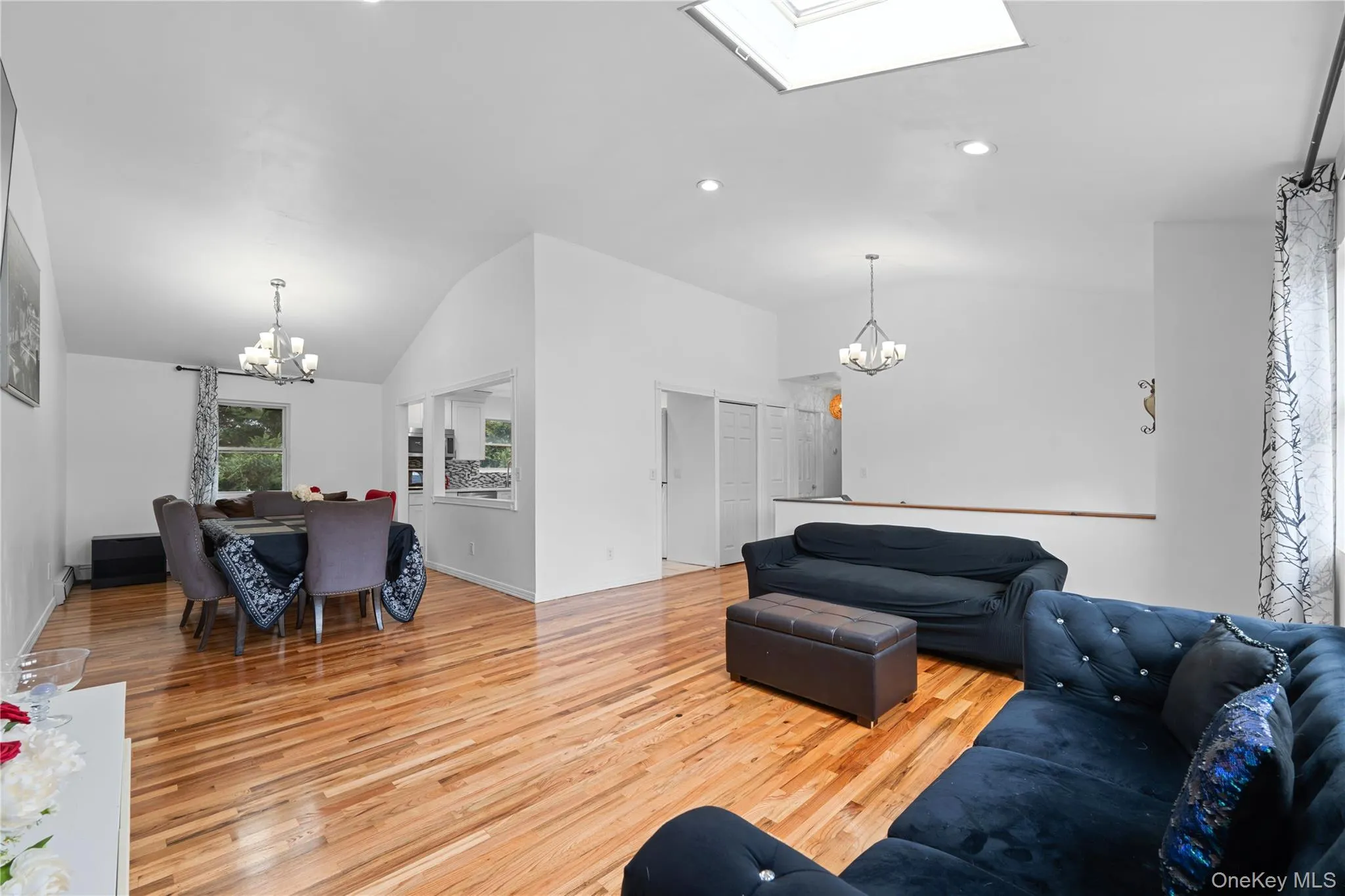 Living room with a chandelier, light wood-type flooring, vaulted ceiling, a skylight, and recessed lighting Living room with a chandelier, light wood-type flooring, vaulted ceiling, a skylight, and recessed lighting