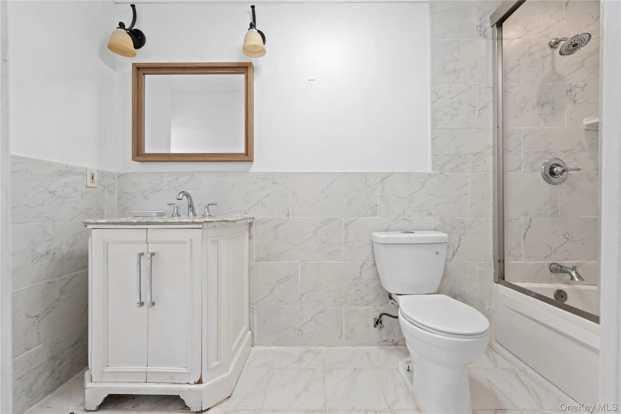 Bathroom featuring tile walls, vanity, shower / tub combination, marble finish floors, and a wainscoted wall Bathroom featuring tile walls, vanity, shower / tub combination, marble finish floors, and a wainscoted wall