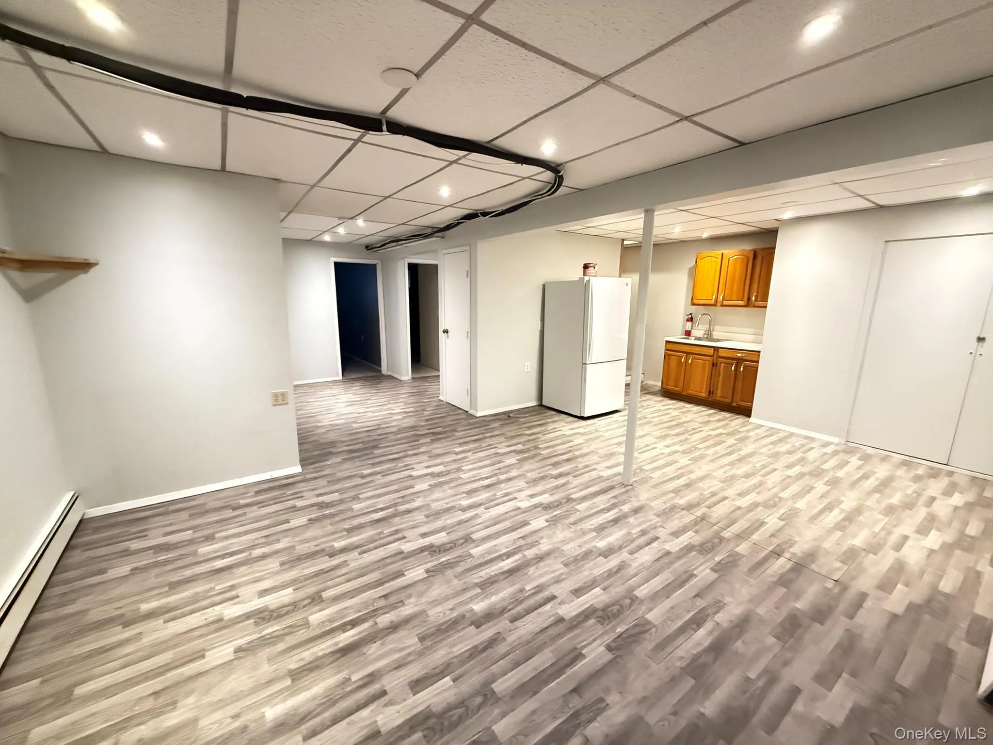 Finished basement with light wood-style floors, a baseboard radiator, a paneled ceiling, freestanding refrigerator, and recessed lighting Finished basement with light wood-style floors, a baseboard radiator, a paneled ceiling, freestanding refrigerator, and recessed lighting