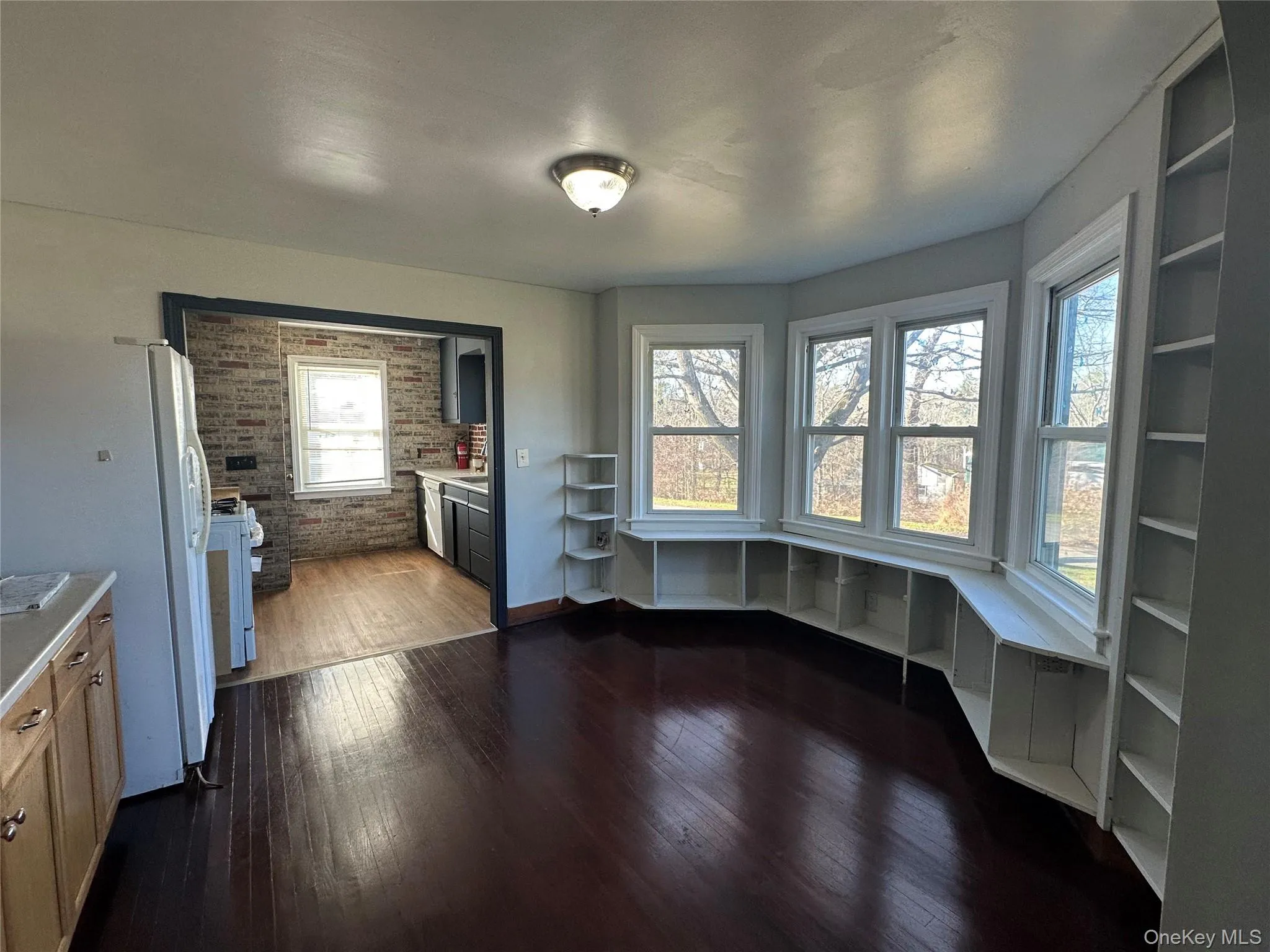 Unfurnished dining area with brick wall, dark wood-style floors, and built in study area Unfurnished dining area with brick wall, dark wood-style floors, and built in study area