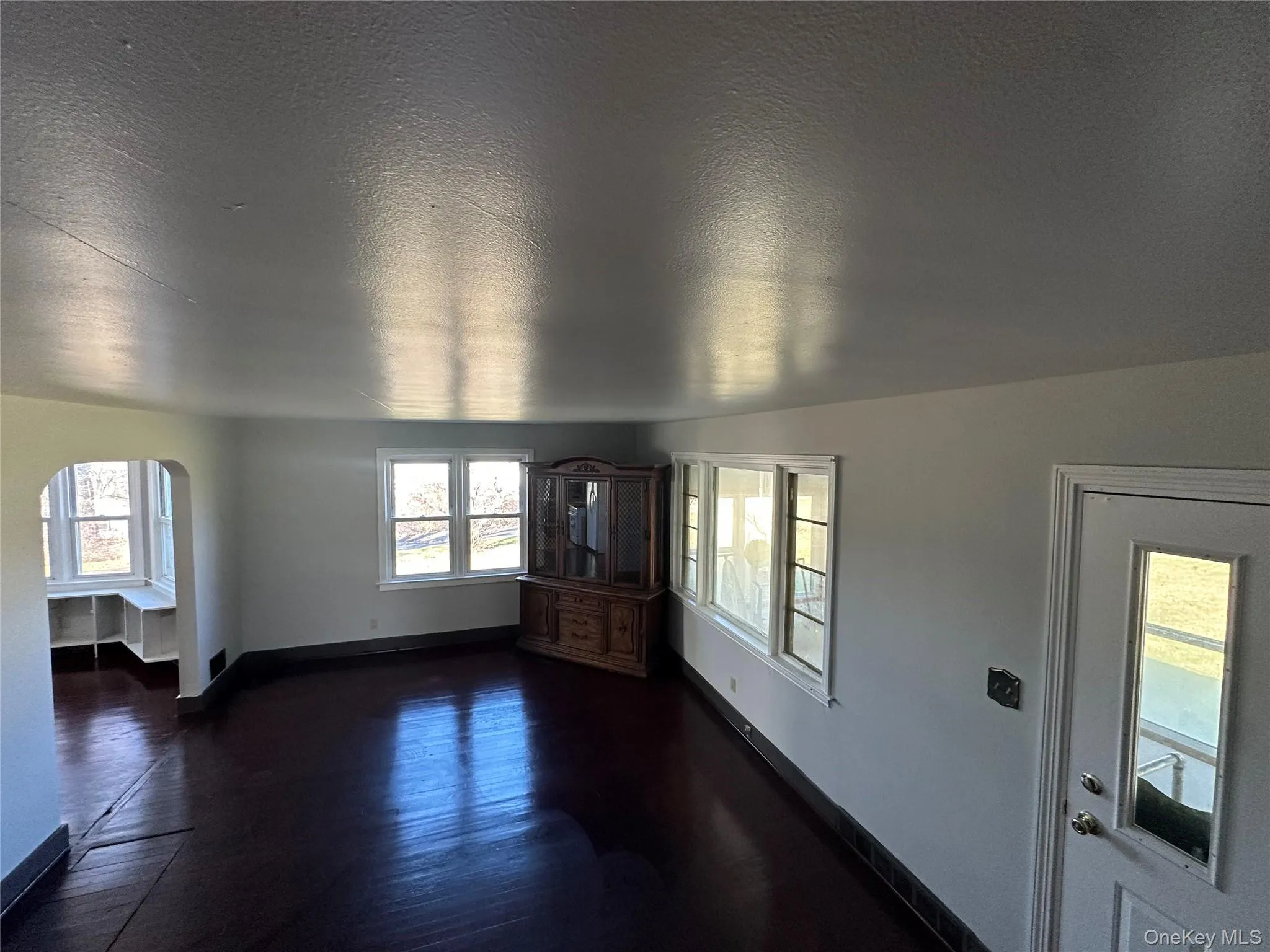 Unfurnished living room with arched walkways, a textured ceiling, and dark wood-style flooring Unfurnished living room with arched walkways, a textured ceiling, and dark wood-style flooring