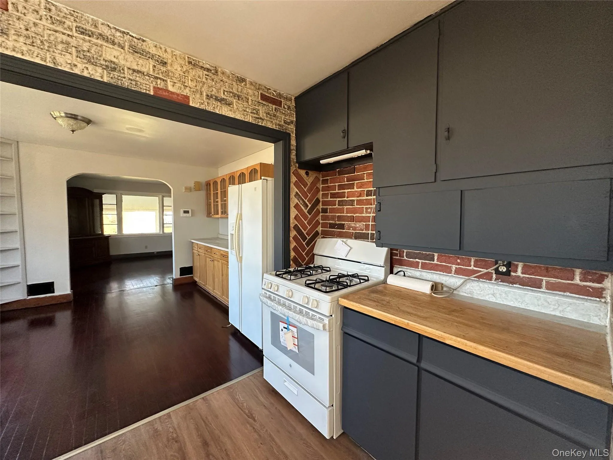 Kitchen featuring white appliances, arched walkways, dark wood-style flooring, gray cabinets, and wooden counters Kitchen featuring white appliances, arched walkways, dark wood-style flooring, gray cabinets, and wooden counters