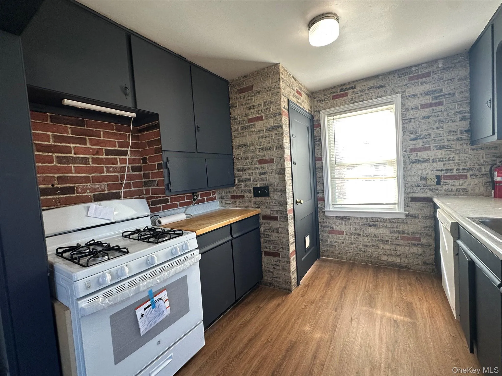 Kitchen with white appliances, dark wood-type flooring, under cabinet range hood, and brick wall Kitchen with white appliances, dark wood-type flooring, under cabinet range hood, and brick wall