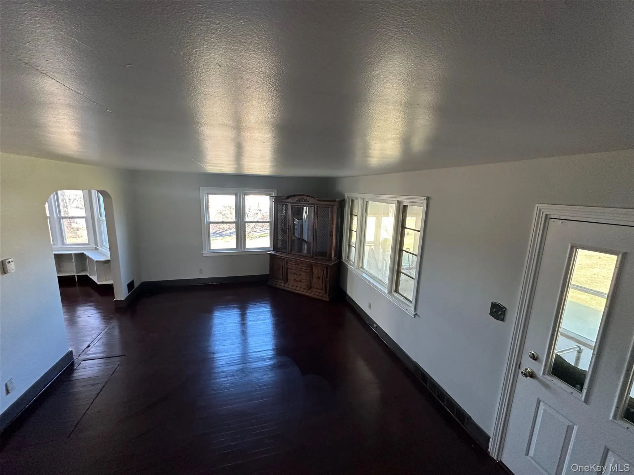 Unfurnished living room with arched walkways, a textured ceiling, and dark wood-style floors Unfurnished living room with arched walkways, a textured ceiling, and dark wood-style floors
