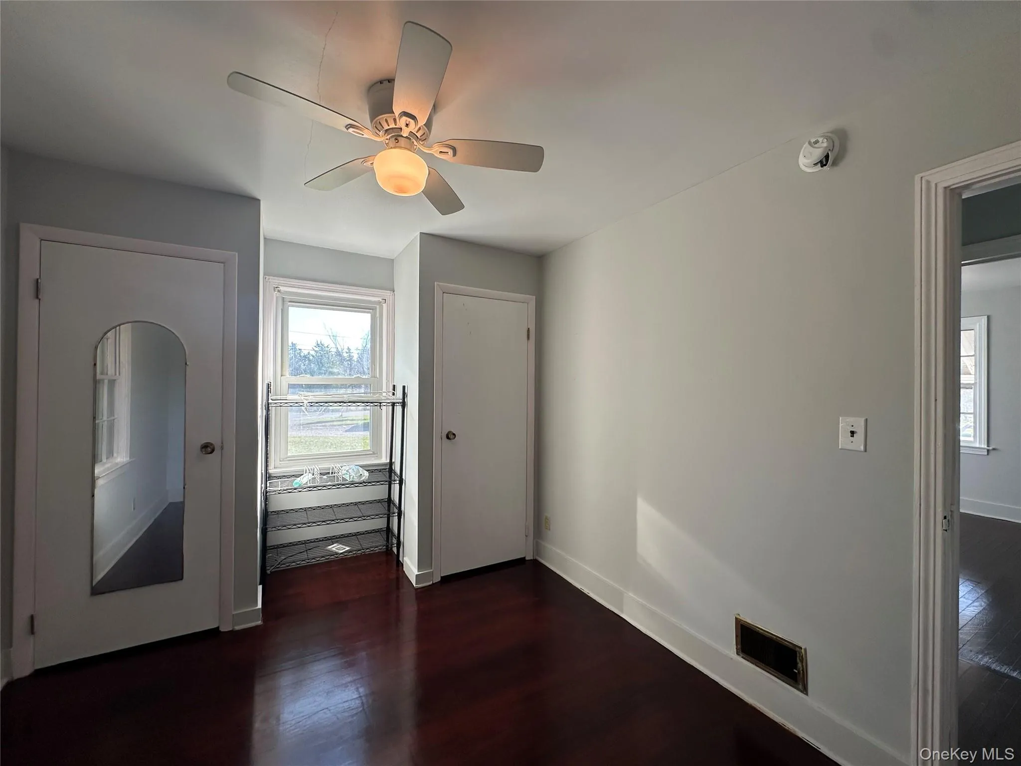 Unfurnished bedroom with dark wood-type flooring, a ceiling fan, and two closets Unfurnished bedroom with dark wood-type flooring, a ceiling fan, and two closets