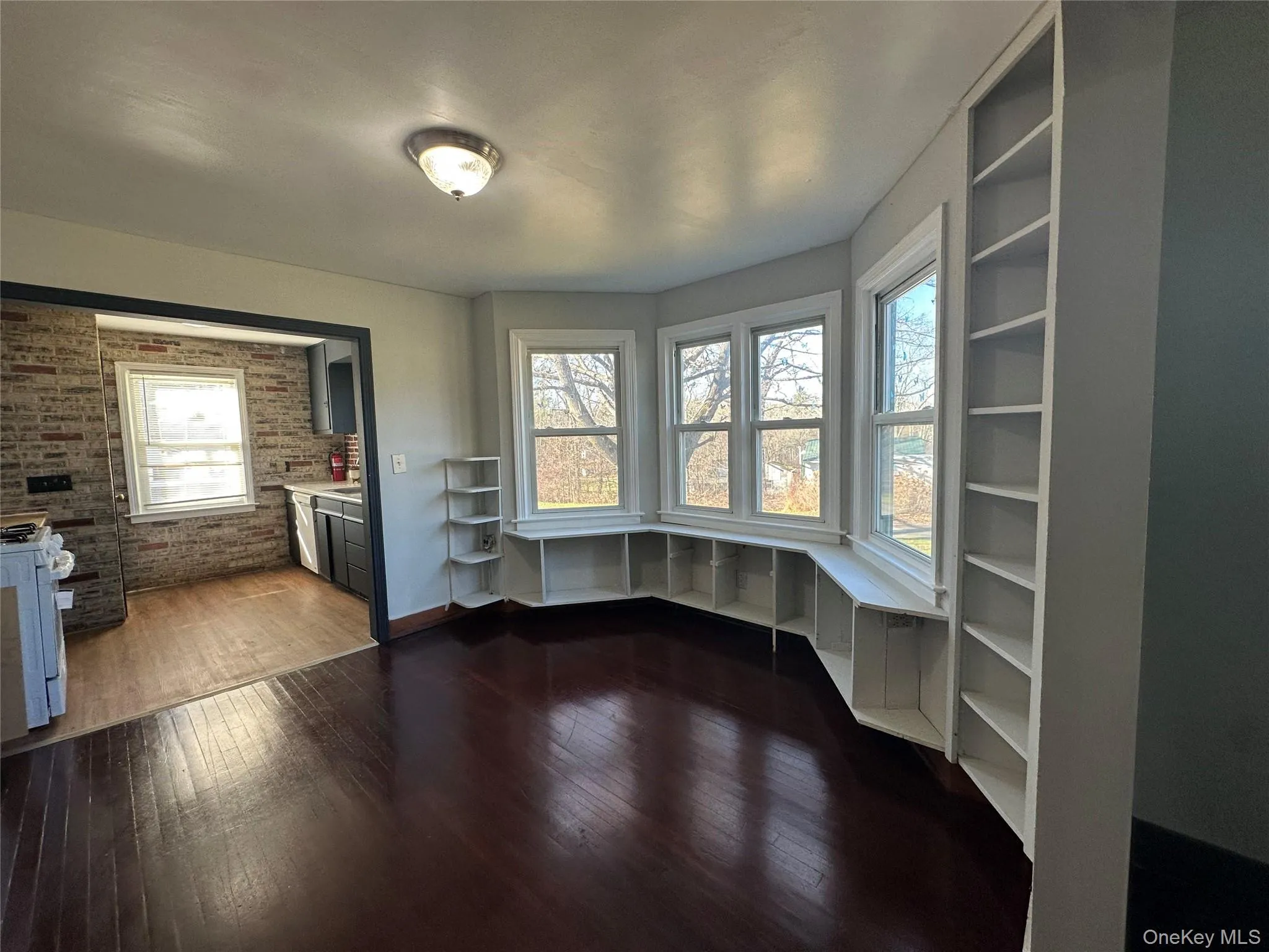 Unfurnished dining area with brick wall, built in study area, and dark wood-style flooring Unfurnished dining area with brick wall, built in study area, and dark wood-style flooring