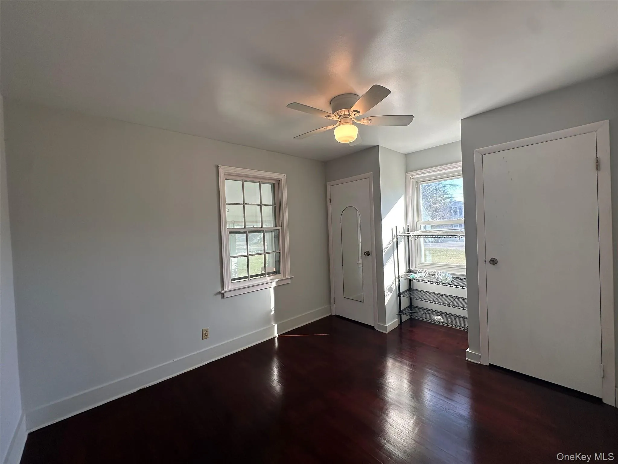 Unfurnished bedroom featuring dark wood-style flooring, multiple closets, and a ceiling fan Unfurnished bedroom featuring dark wood-style flooring, multiple closets, and a ceiling fan