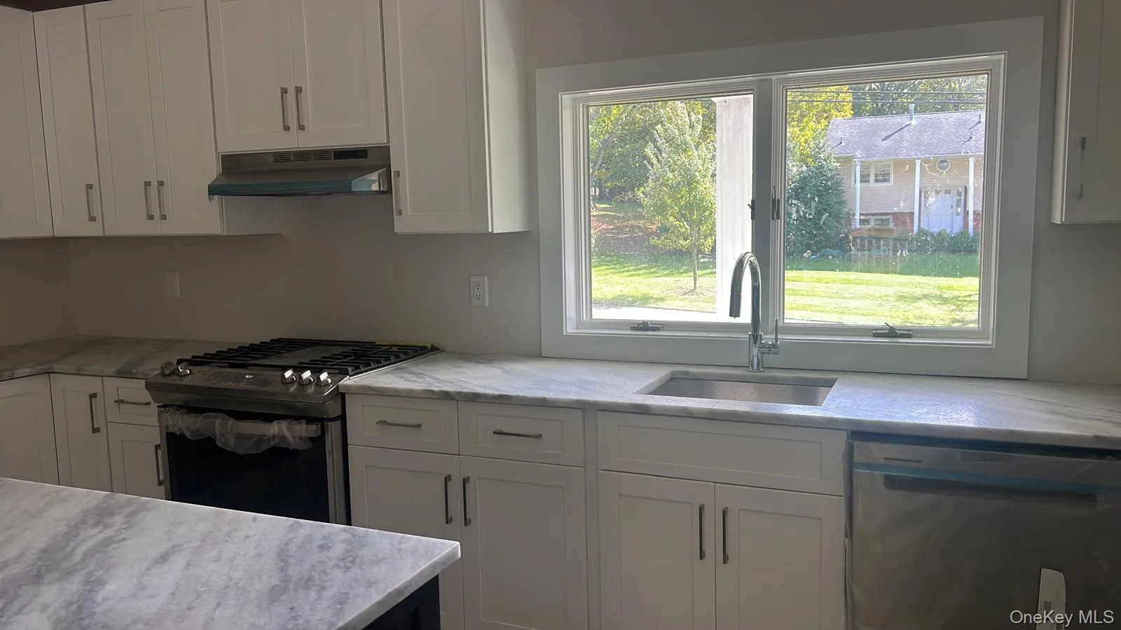 Kitchen featuring white cabinetry, appliances with stainless steel finishes, light stone counters, and under cabinet range hood Kitchen featuring white cabinetry, appliances with stainless steel finishes, light stone counters, and under cabinet range hood
