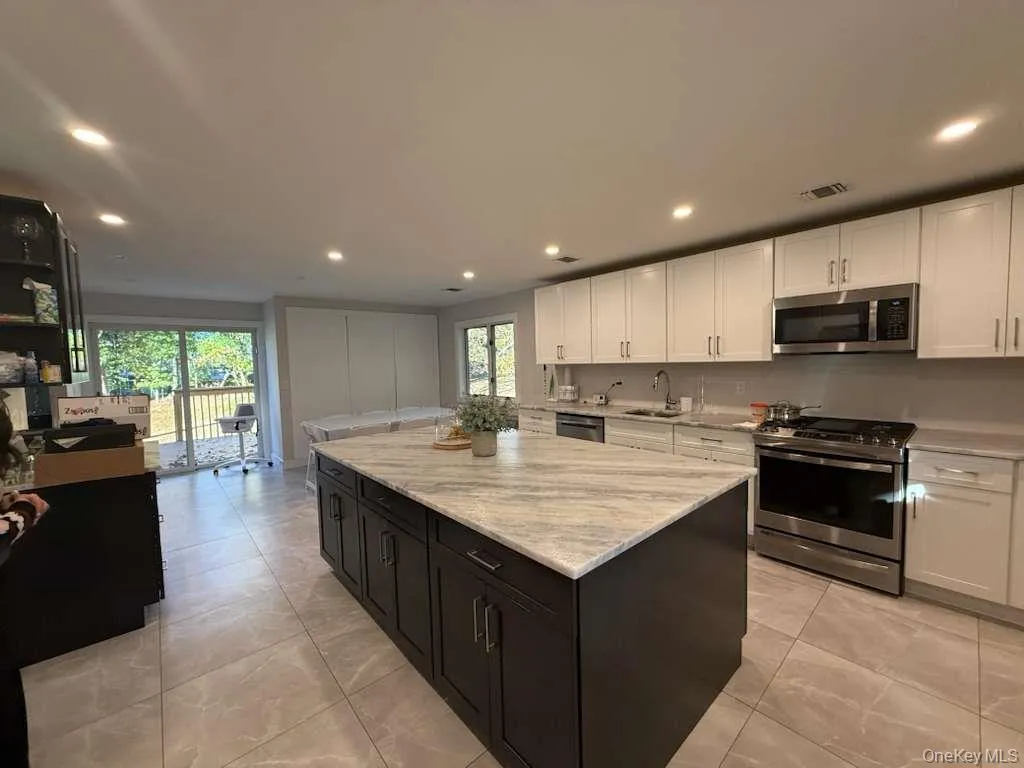Kitchen featuring appliances with stainless steel finishes, recessed lighting, white cabinets, a kitchen island, and light stone counters Kitchen featuring appliances with stainless steel finishes, recessed lighting, white cabinets, a kitchen island, and light stone counters