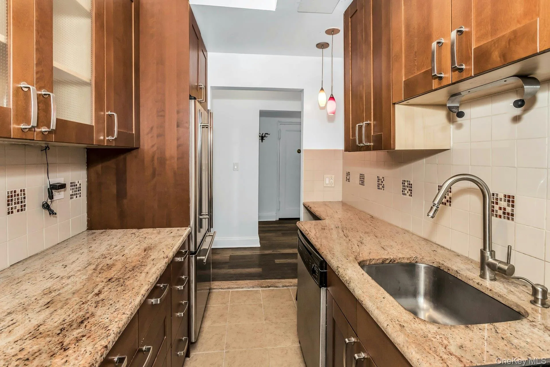 Kitchen with decorative backsplash, decorative light fixtures, light stone countertops, and brown cabinetry Kitchen with decorative backsplash, decorative light fixtures, light stone countertops, and brown cabinetry