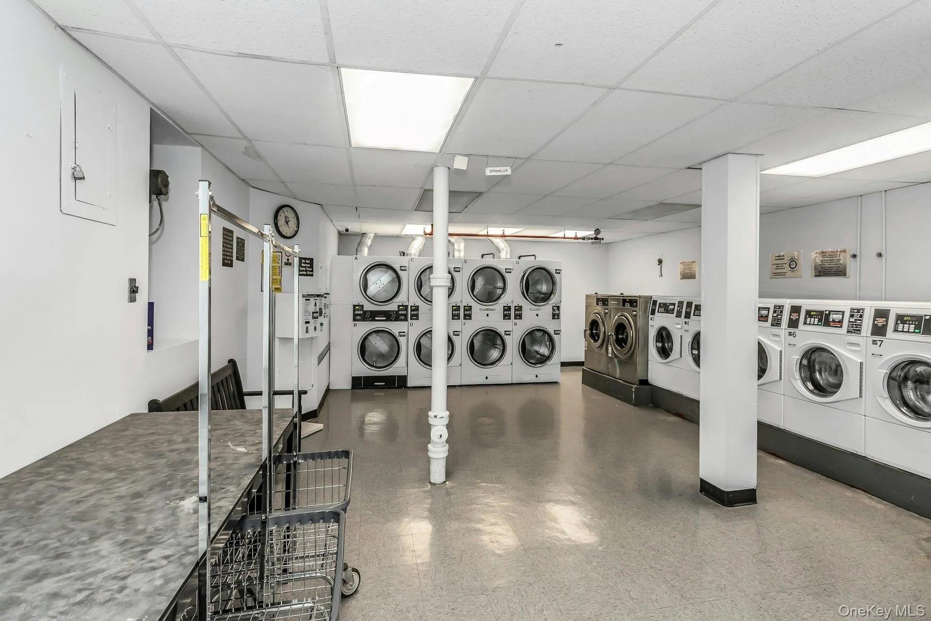 Shared laundry room with a drop ceiling, independent washer and dryer, electric panel, and stacked washing machine and dryer Shared laundry room with a drop ceiling, independent washer and dryer, electric panel, and stacked washing machine and dryer