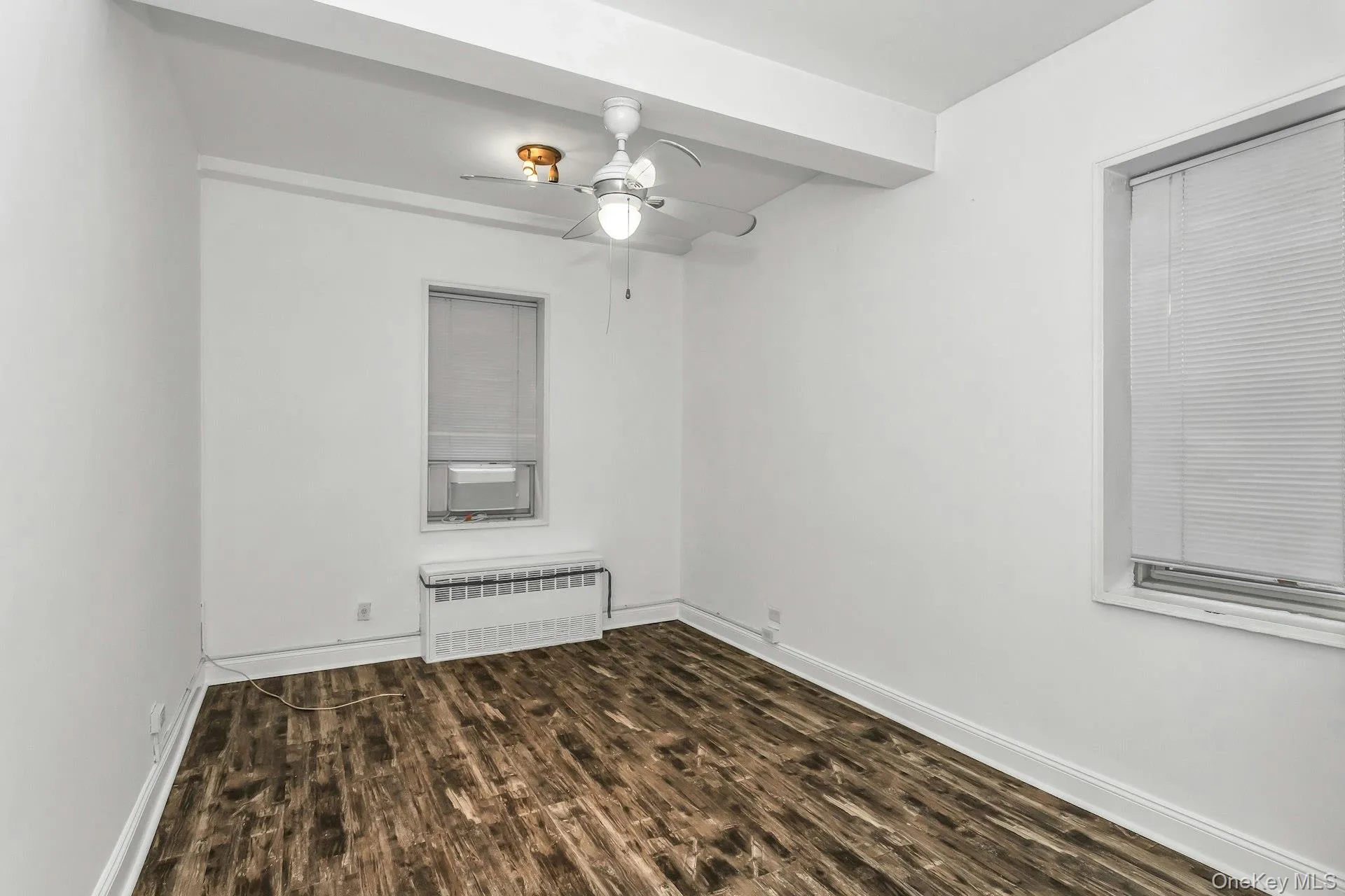 Unfurnished room with radiator heating unit, dark wood finished floors, a ceiling fan, beamed ceiling, and cooling unit Unfurnished room with radiator heating unit, dark wood finished floors, a ceiling fan, beamed ceiling, and cooling unit