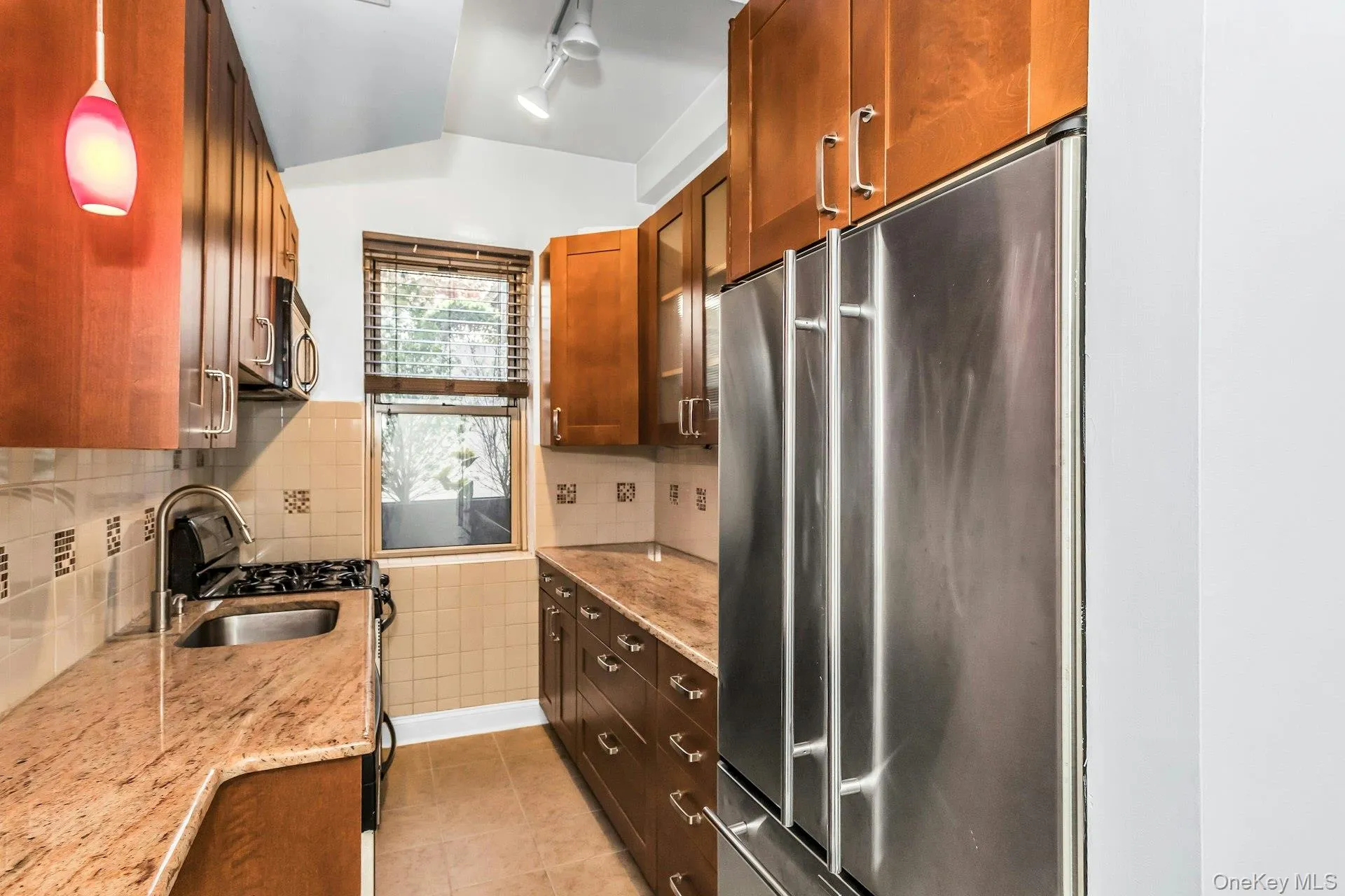 Kitchen with light stone counters, stainless steel appliances, light tile patterned flooring, decorative backsplash, and lofted ceiling Kitchen with light stone counters, stainless steel appliances, light tile patterned flooring, decorative backsplash, and lofted ceiling
