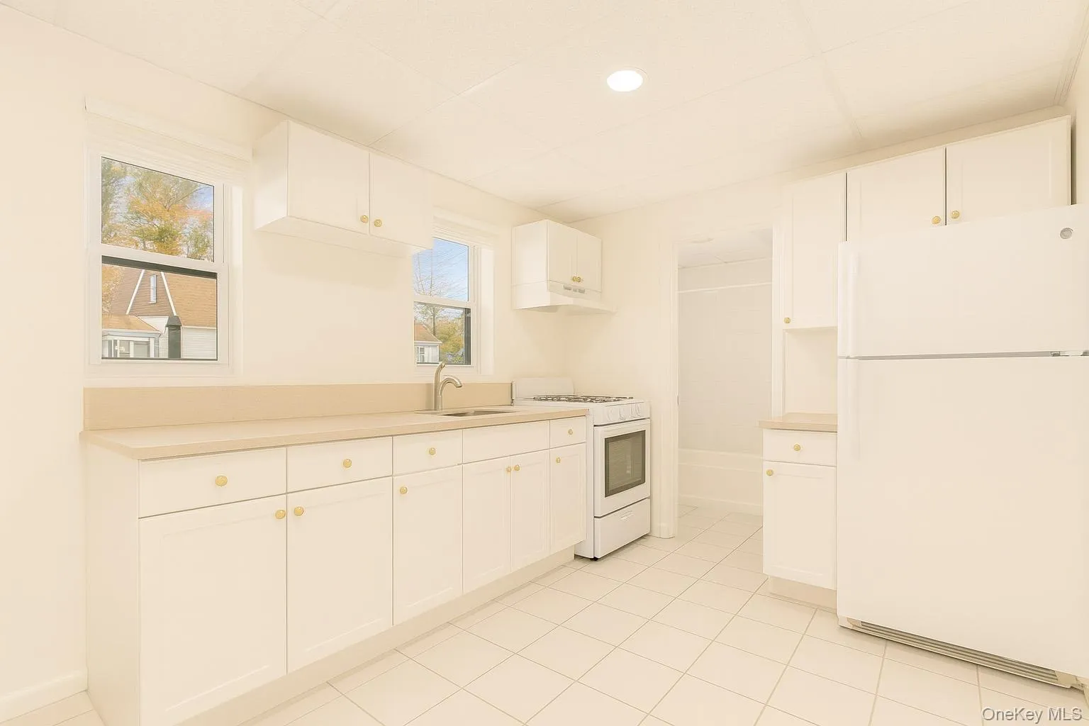 Kitchen with white appliances, white cabinets, light countertops, light tile patterned floors, and under cabinet range hood Kitchen with white appliances, white cabinets, light countertops, light tile patterned floors, and under cabinet range hood