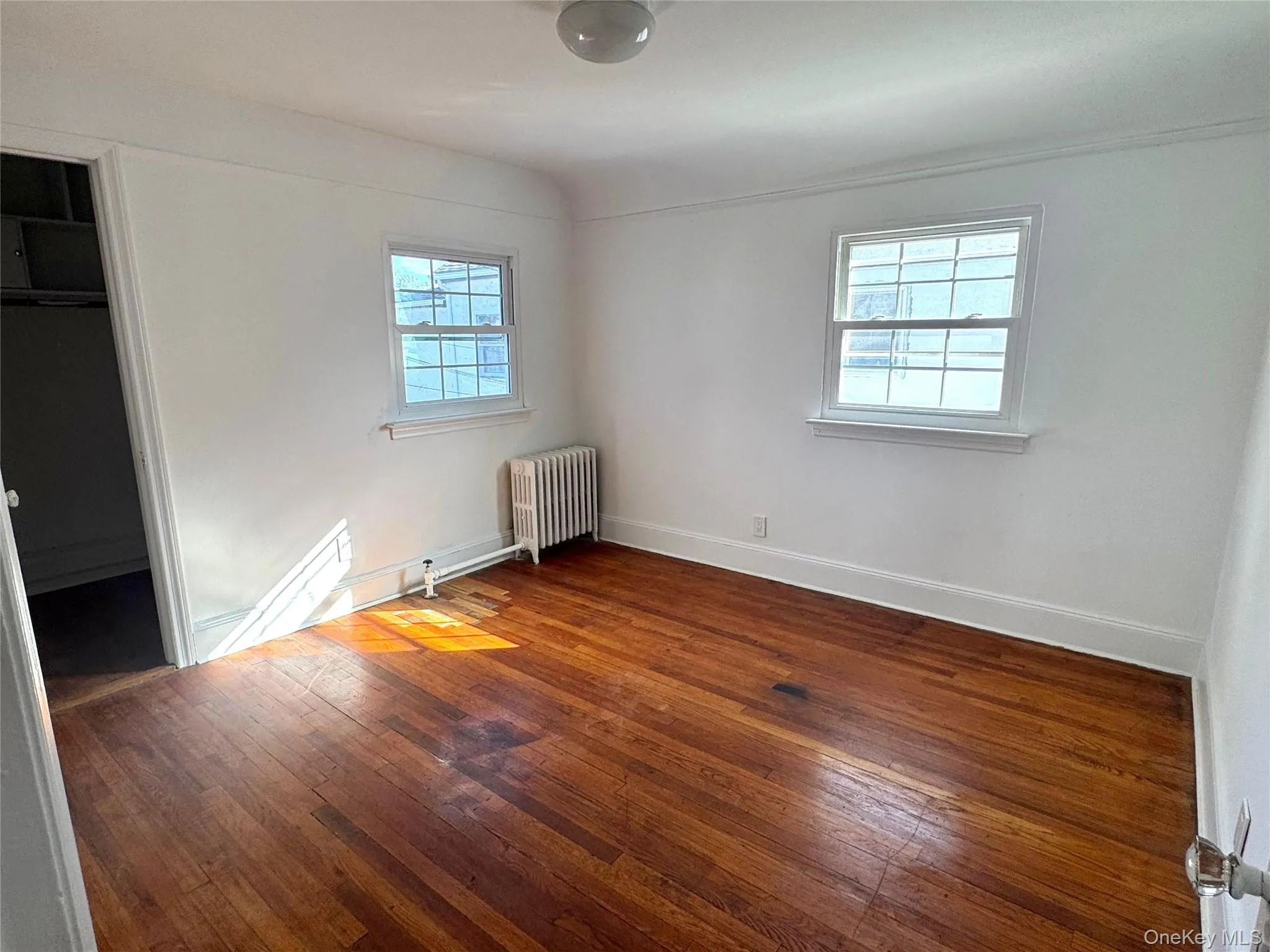 Unfurnished bedroom featuring hardwood / wood-style floors, radiator heating unit, and a spacious closet Unfurnished bedroom featuring hardwood / wood-style floors, radiator heating unit, and a spacious closet