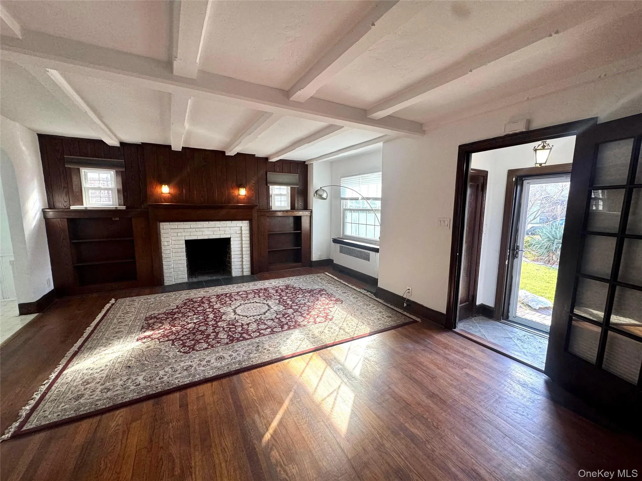 Unfurnished living room with wooden walls, a fireplace, beam ceiling, healthy amount of natural light, and wood finished floors Unfurnished living room with wooden walls, a fireplace, beam ceiling, healthy amount of natural light, and wood finished floors