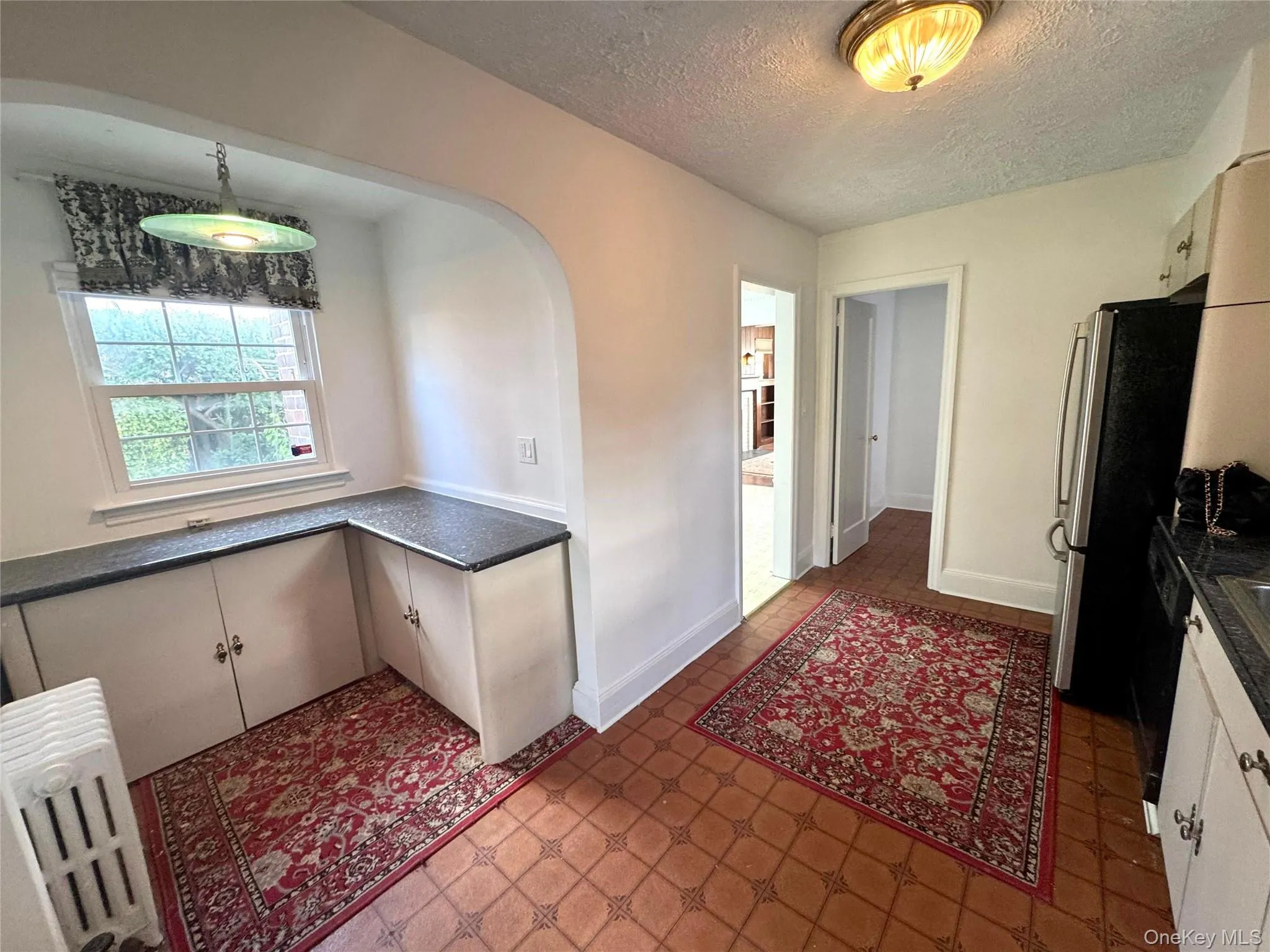 Kitchen with radiator heating unit, a textured ceiling, freestanding refrigerator, white cabinets, and arched walkways Kitchen with radiator heating unit, a textured ceiling, freestanding refrigerator, white cabinets, and arched walkways