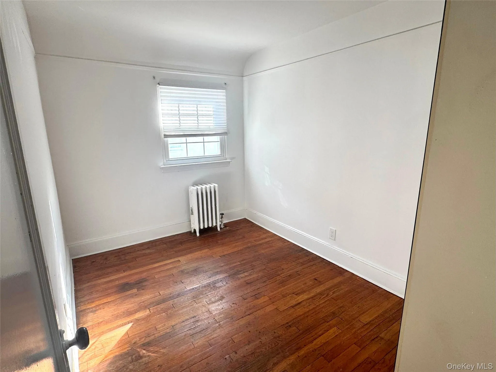 Unfurnished room with radiator heating unit and dark wood-style flooring Unfurnished room with radiator heating unit and dark wood-style flooring