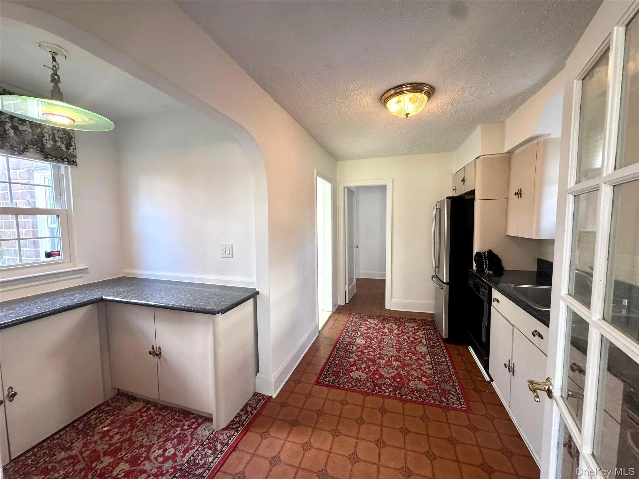 Kitchen featuring dark flooring, dark countertops, arched walkways, a textured ceiling, and freestanding refrigerator Kitchen featuring dark flooring, dark countertops, arched walkways, a textured ceiling, and freestanding refrigerator