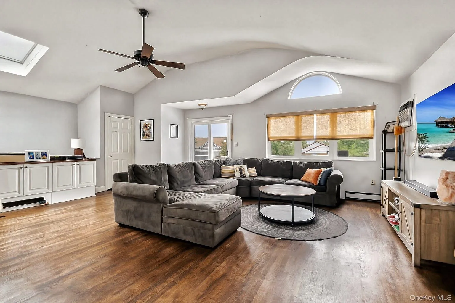 Living area featuring a skylight, a ceiling fan, wood finished floors, lofted ceiling, and a baseboard radiator Living area featuring a skylight, a ceiling fan, wood finished floors, lofted ceiling, and a baseboard radiator