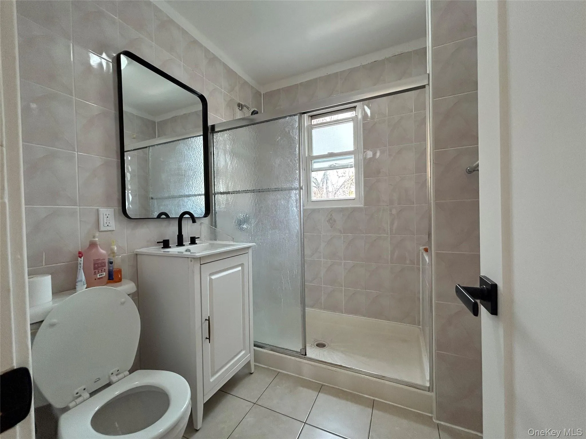 Bathroom featuring a stall shower, vanity, light tile patterned flooring, and tile walls Bathroom featuring a stall shower, vanity, light tile patterned flooring, and tile walls