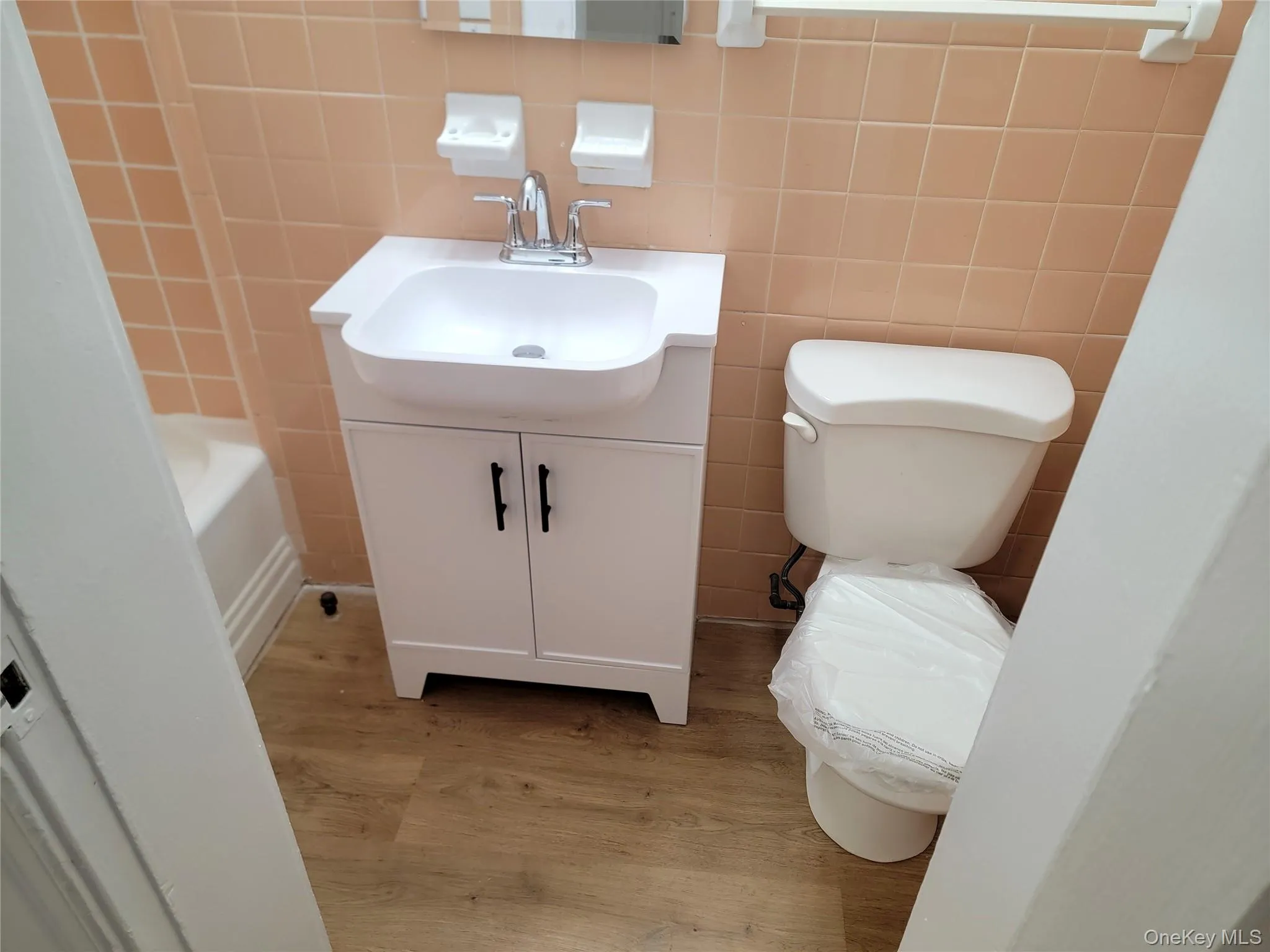 Bathroom with vanity, light wood-type flooring, tile walls, and a tub Bathroom with vanity, light wood-type flooring, tile walls, and a tub