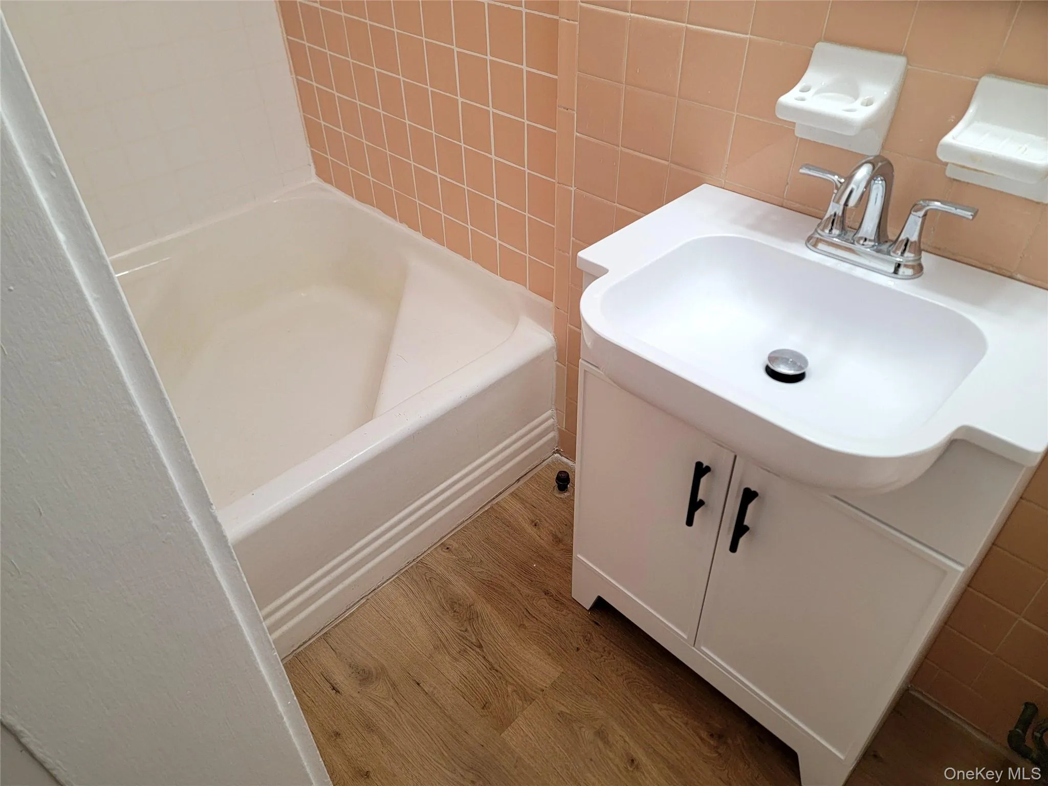 Bathroom featuring tile walls, vanity, light wood-style floors, shower / washtub combination, and decorative backsplash Bathroom featuring tile walls, vanity, light wood-style floors, shower / washtub combination, and decorative backsplash