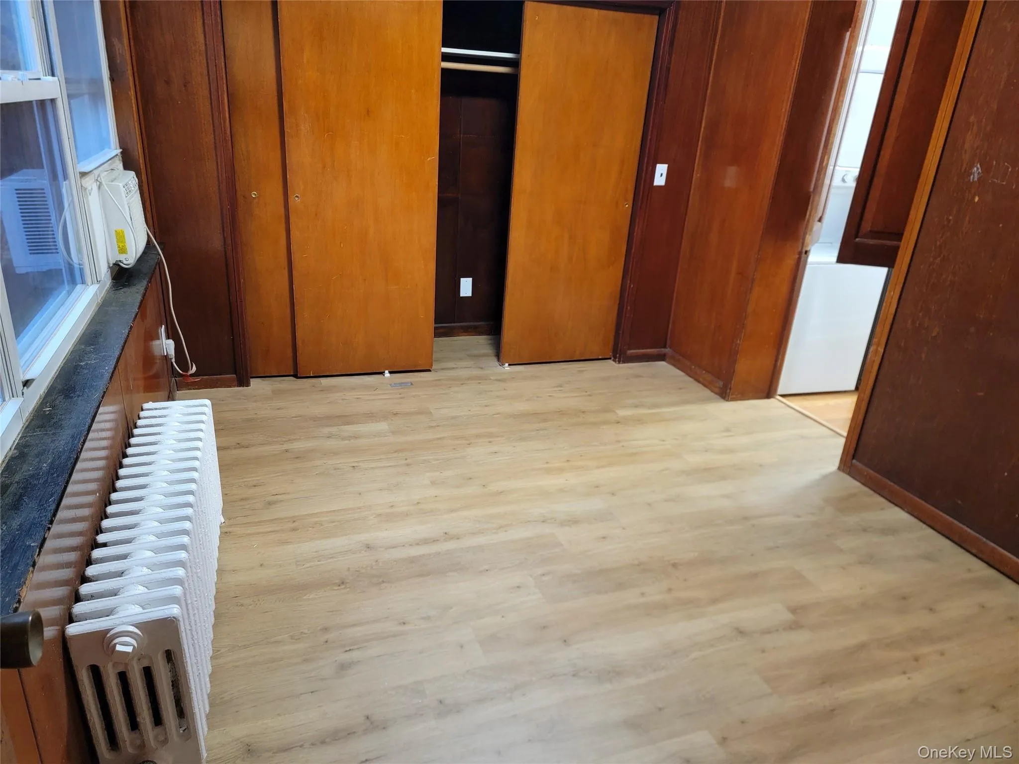 Unfurnished bedroom featuring radiator heating unit, light wood finished floors, a closet, and cooling unit Unfurnished bedroom featuring radiator heating unit, light wood finished floors, a closet, and cooling unit