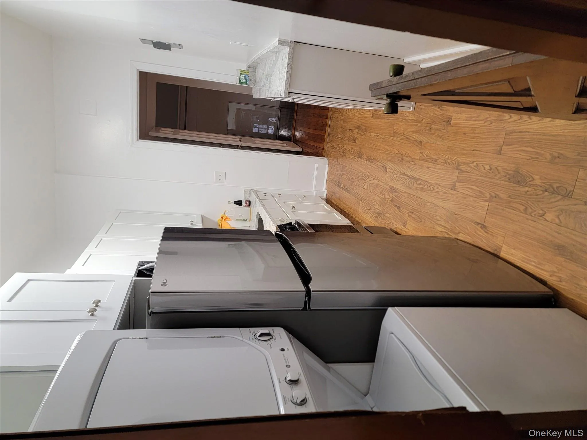 Kitchen featuring white cabinets, light wood-type flooring, stacked washer / dryer, light stone countertops, and refrigerator Kitchen featuring white cabinets, light wood-type flooring, stacked washer / dryer, light stone countertops, and refrigerator