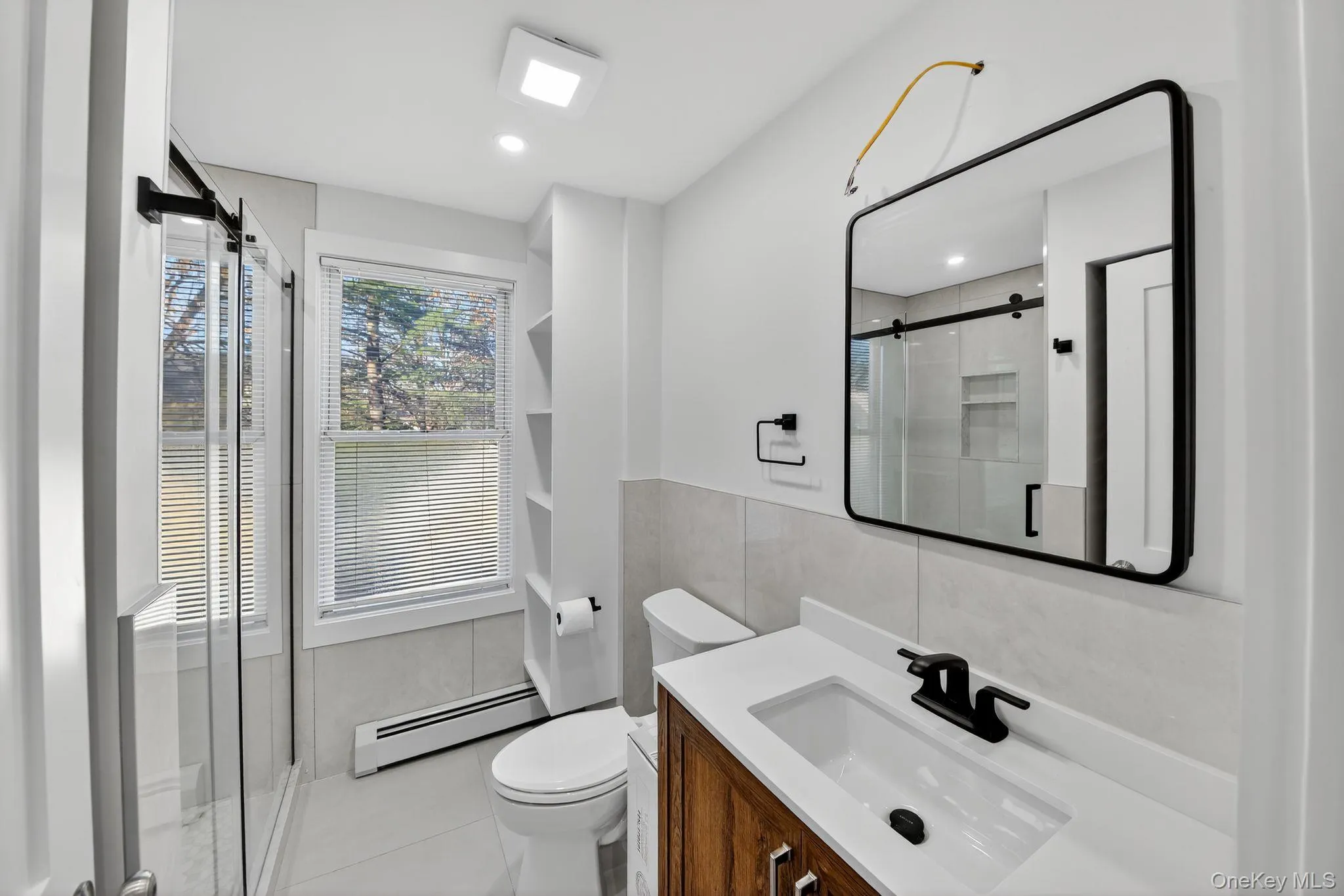 Bathroom featuring vanity, a stall shower, a baseboard heating unit, tile walls, and light tile patterned flooring Bathroom featuring vanity, a stall shower, a baseboard heating unit, tile walls, and light tile patterned flooring