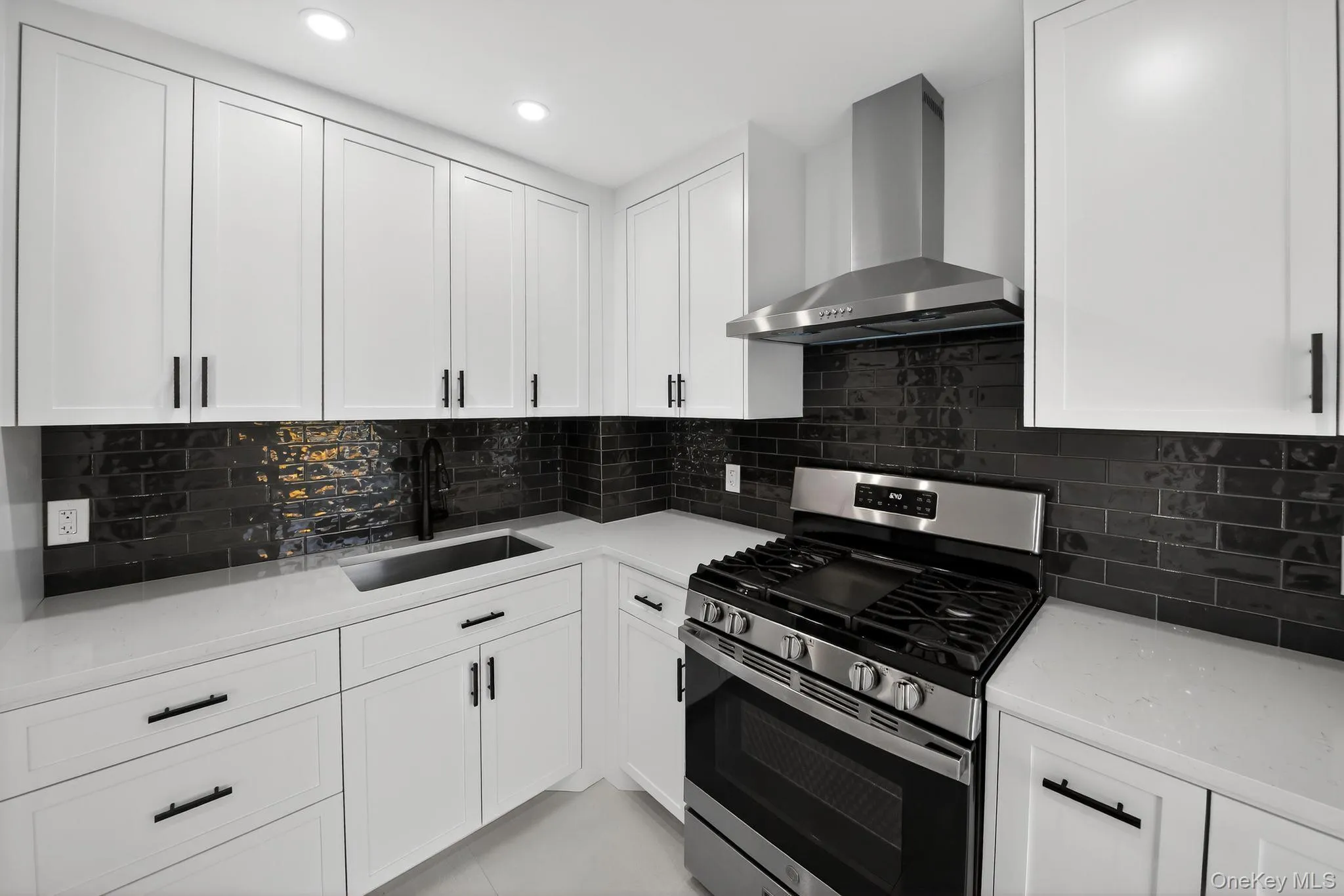Kitchen with stainless steel gas range oven, wall chimney exhaust hood, white cabinetry, light stone counters, and recessed lighting Kitchen with stainless steel gas range oven, wall chimney exhaust hood, white cabinetry, light stone counters, and recessed lighting