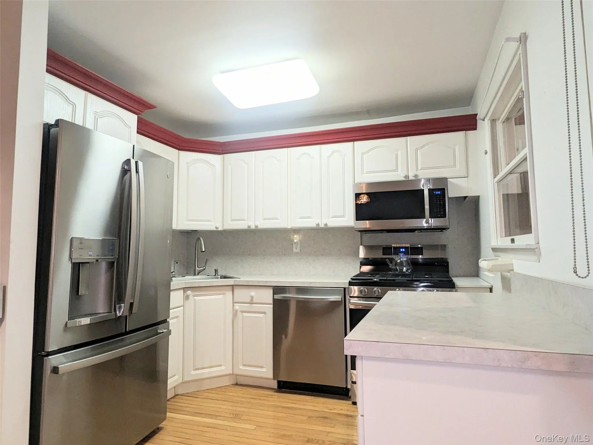 Kitchen with appliances with stainless steel finishes, light countertops, white cabinetry, decorative backsplash, and light wood-style flooring Kitchen with appliances with stainless steel finishes, light countertops, white cabinetry, decorative backsplash, and light wood-style flooring