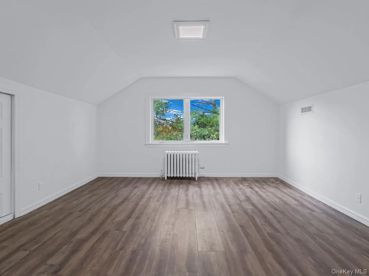 Additional living space featuring vaulted ceiling, dark wood finished floors, and radiator Additional living space featuring vaulted ceiling, dark wood finished floors, and radiator