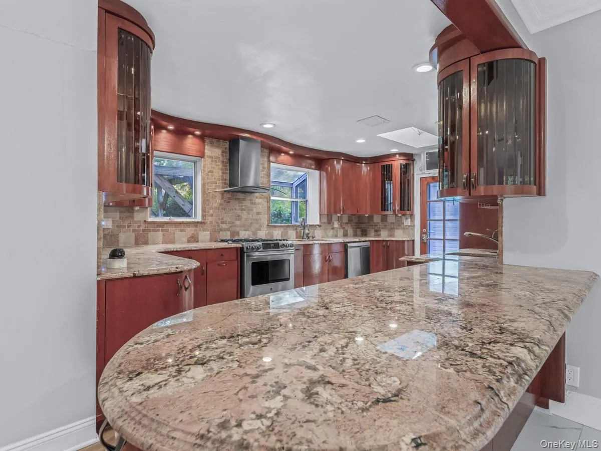 Kitchen featuring glass insert cabinets, a peninsula, light stone countertops, stainless steel appliances, and brown cabinets Kitchen featuring glass insert cabinets, a peninsula, light stone countertops, stainless steel appliances, and brown cabinets