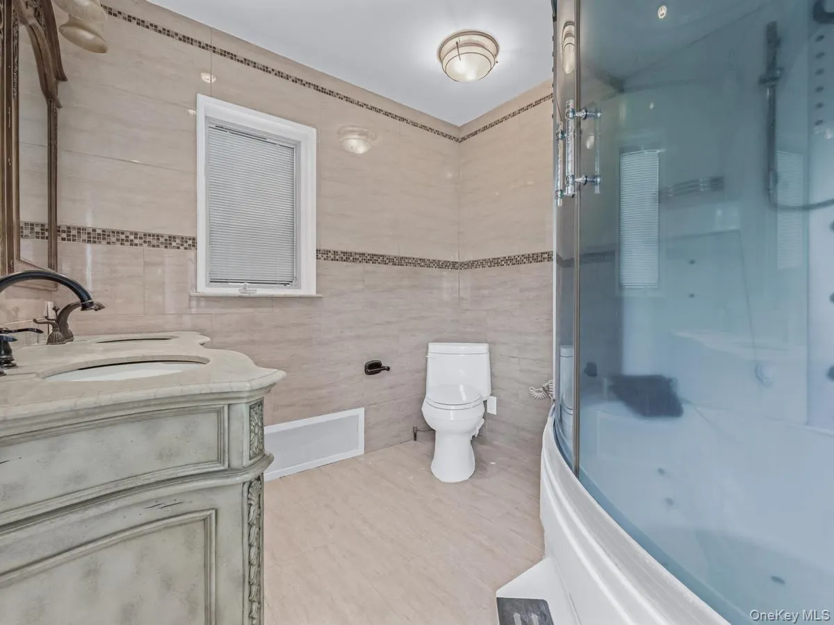 Full bathroom featuring double vanity, tile walls, and shower / bath combination with glass door Full bathroom featuring double vanity, tile walls, and shower / bath combination with glass door