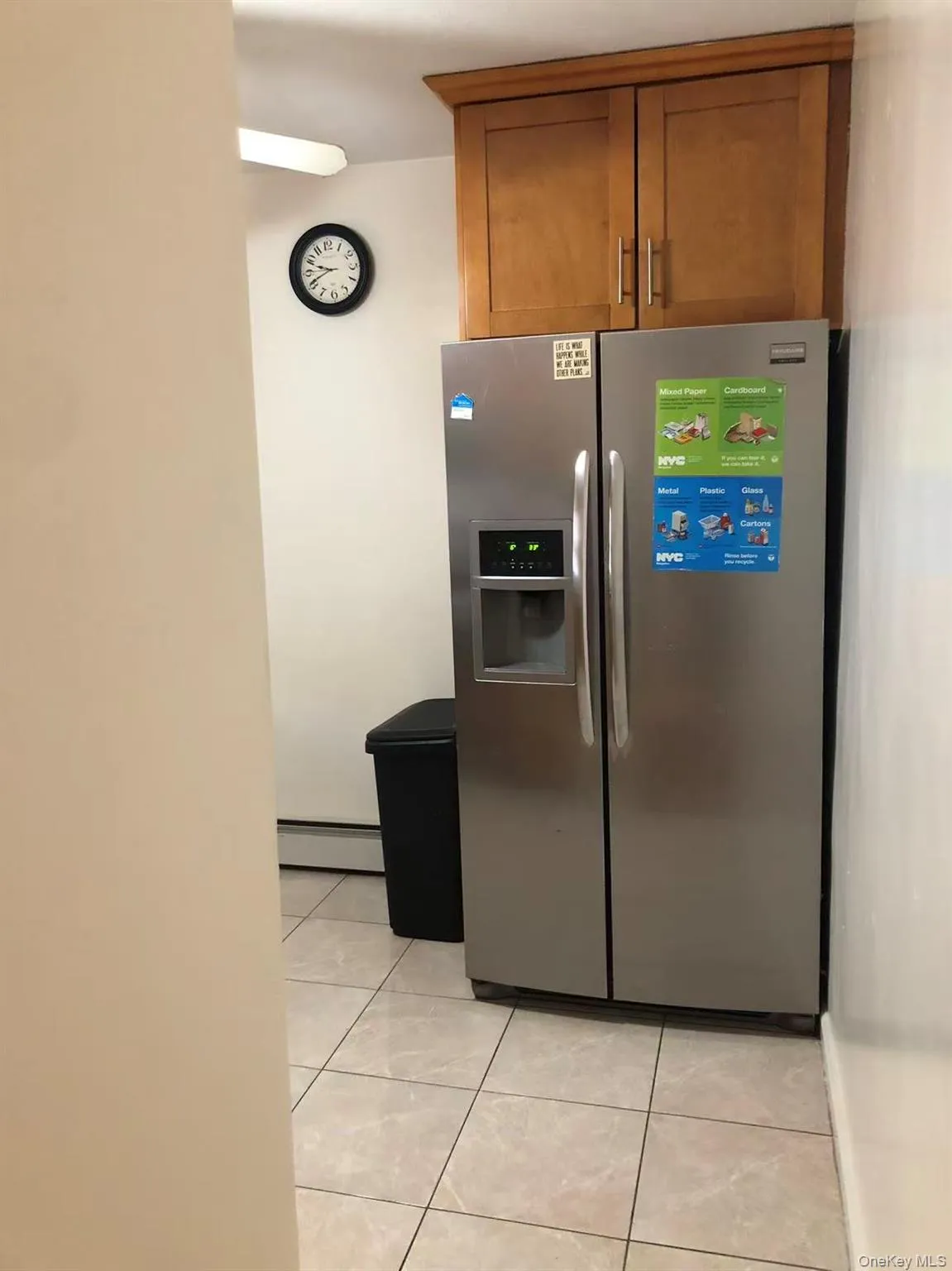 Kitchen with stainless steel fridge with ice dispenser, light tile patterned floors, brown cabinetry, and a baseboard radiator Kitchen with stainless steel fridge with ice dispenser, light tile patterned floors, brown cabinetry, and a baseboard radiator