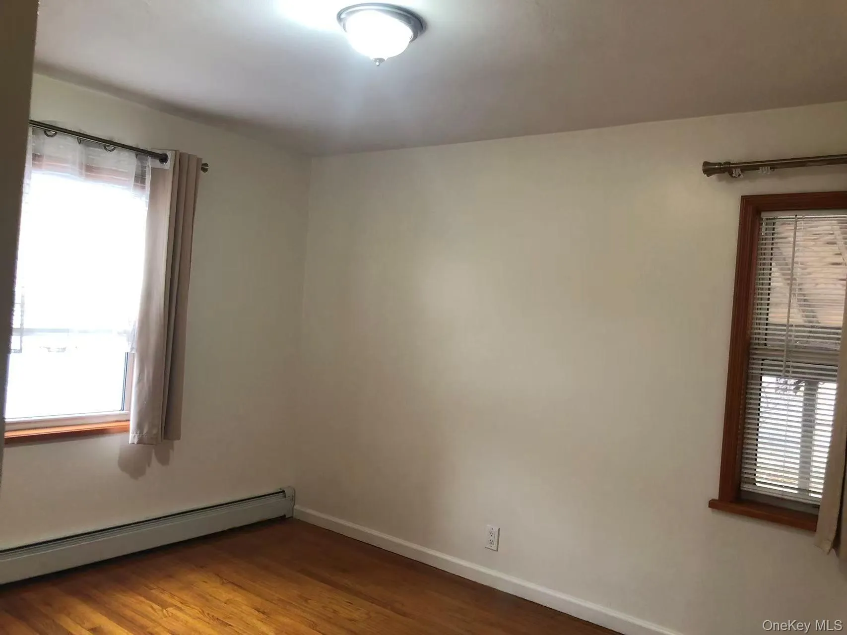 Unfurnished room with plenty of natural light, dark wood-type flooring, and a baseboard heating unit Unfurnished room with plenty of natural light, dark wood-type flooring, and a baseboard heating unit