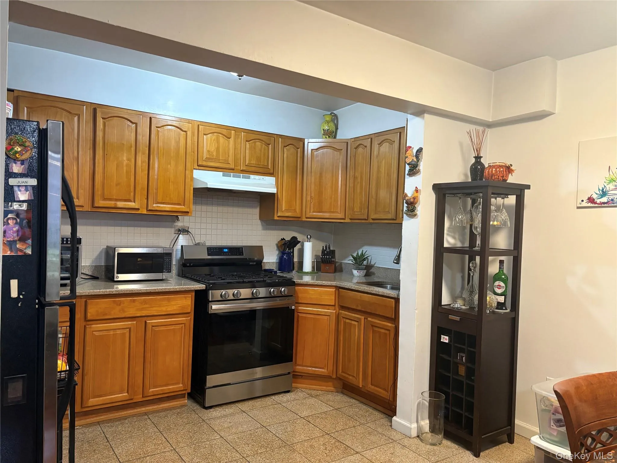 Kitchen with brown cabinetry, appliances with stainless steel finishes, light stone countertops, and decorative backsplash Kitchen with brown cabinetry, appliances with stainless steel finishes, light stone countertops, and decorative backsplash