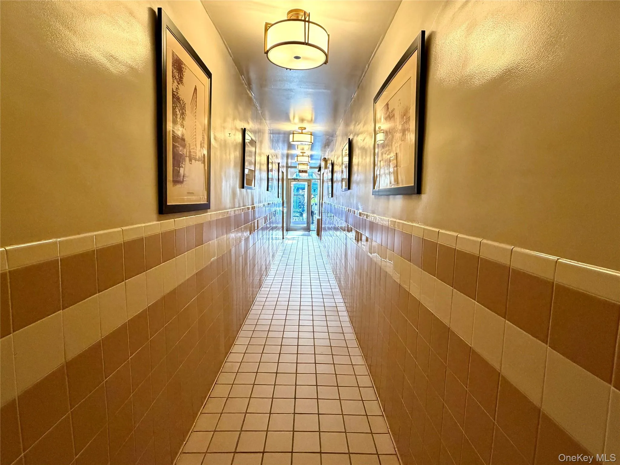 Hallway with tile patterned flooring, a wainscoted wall, and tile walls Hallway with tile patterned flooring, a wainscoted wall, and tile walls