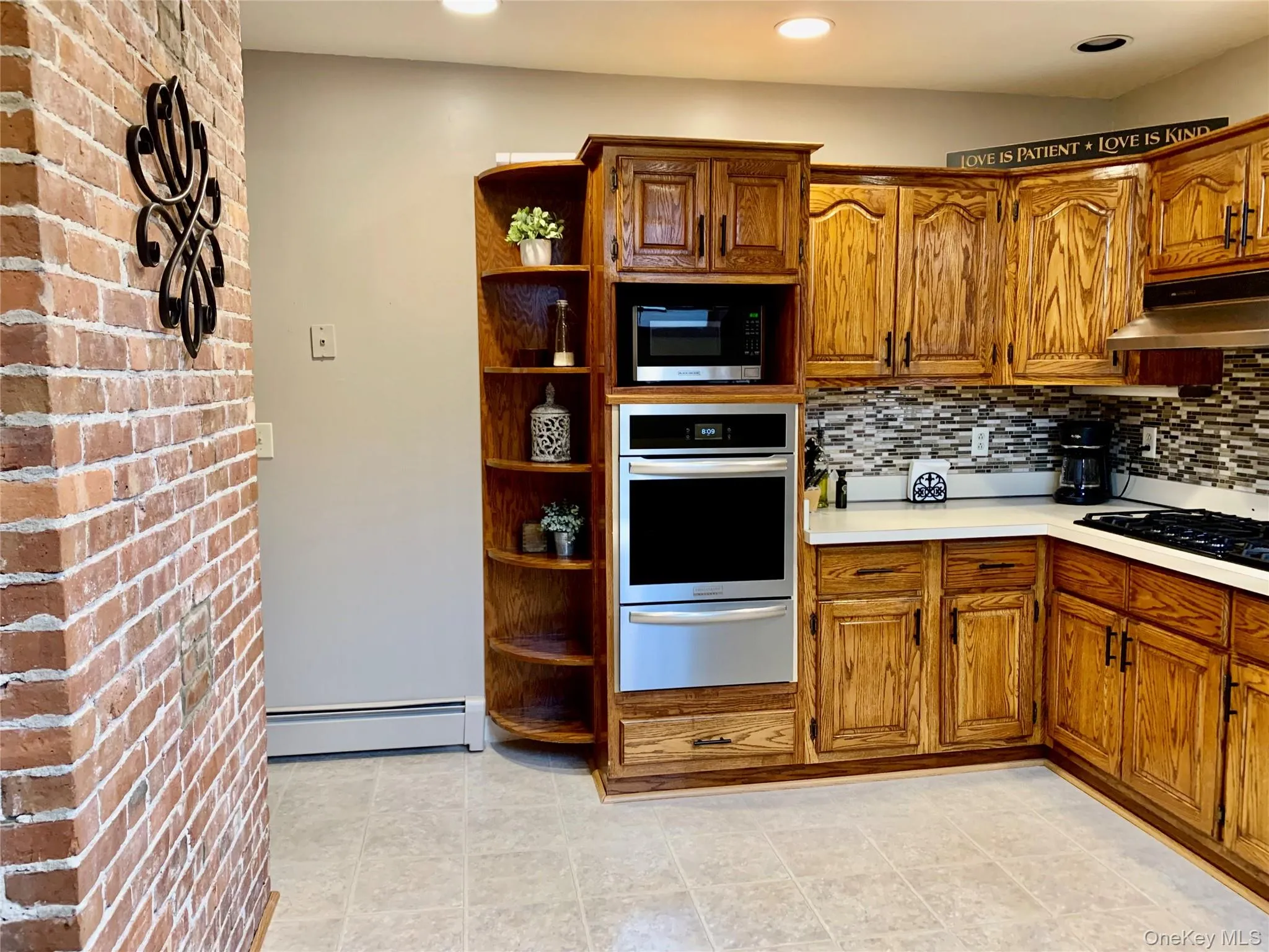 Kitchen featuring open shelves, stainless steel appliances, brown cabinetry, light countertops, and a warming drawer Kitchen featuring open shelves, stainless steel appliances, brown cabinetry, light countertops, and a warming drawer