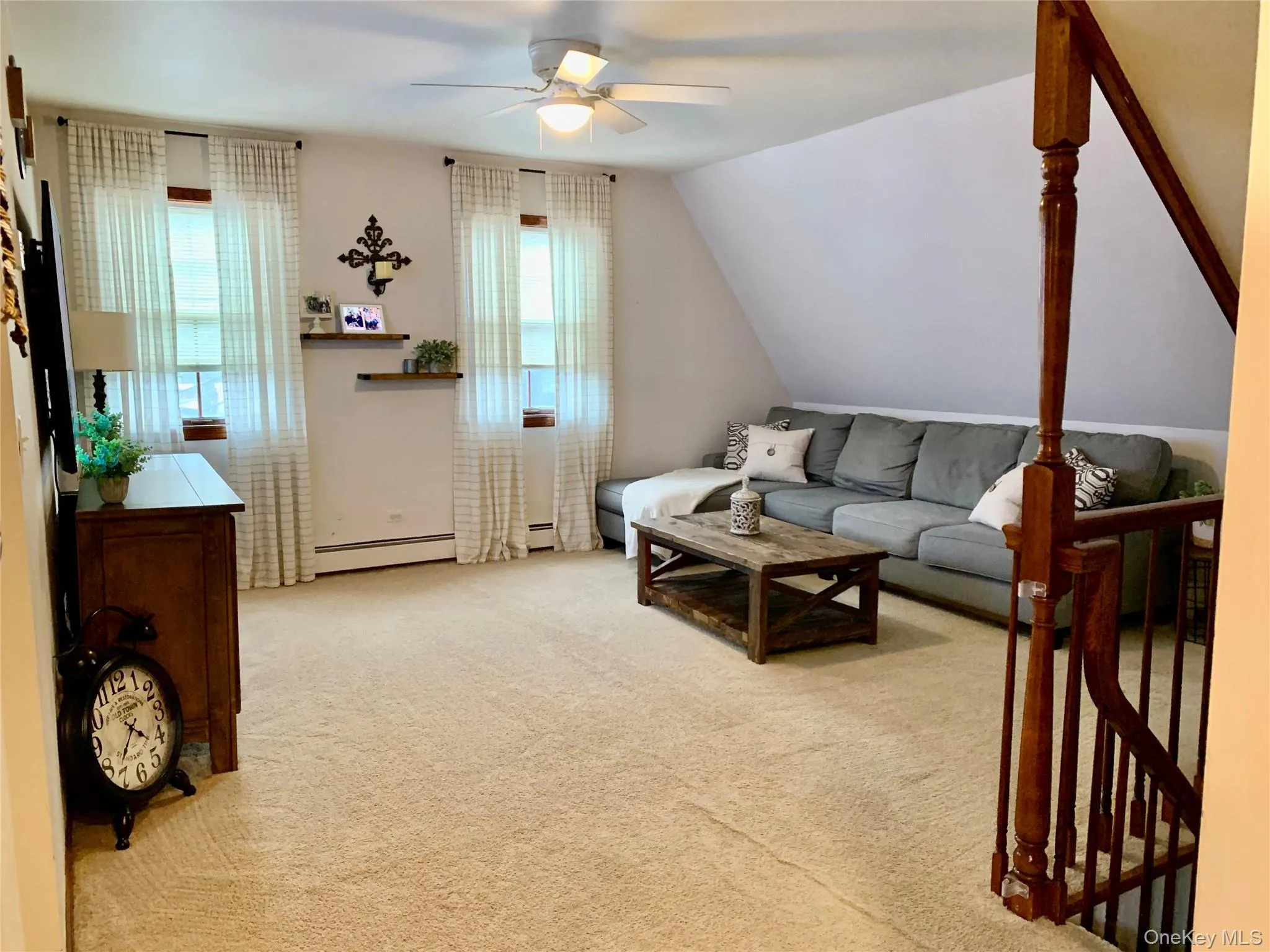 Living area featuring light colored carpet, vaulted ceiling, a ceiling fan, and a baseboard heating unit Living area featuring light colored carpet, vaulted ceiling, a ceiling fan, and a baseboard heating unit
