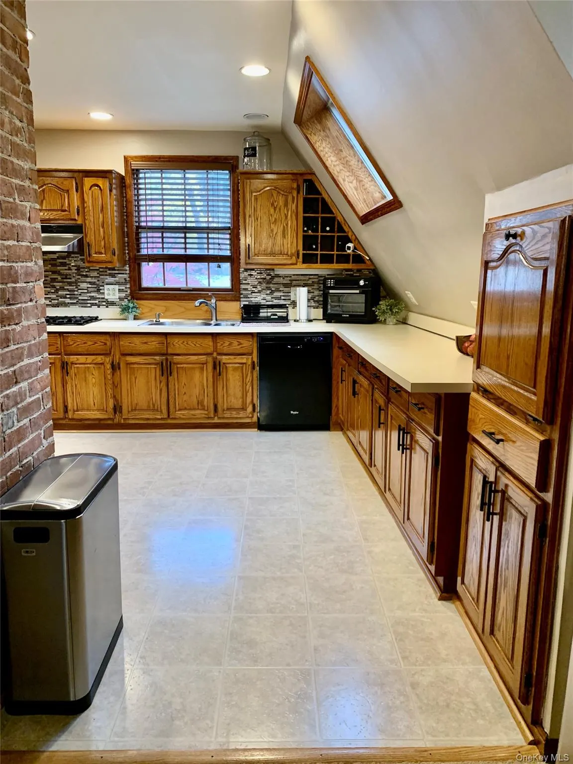 Kitchen with brown cabinetry, a skylight, light countertops, dishwasher, and recessed lighting Kitchen with brown cabinetry, a skylight, light countertops, dishwasher, and recessed lighting